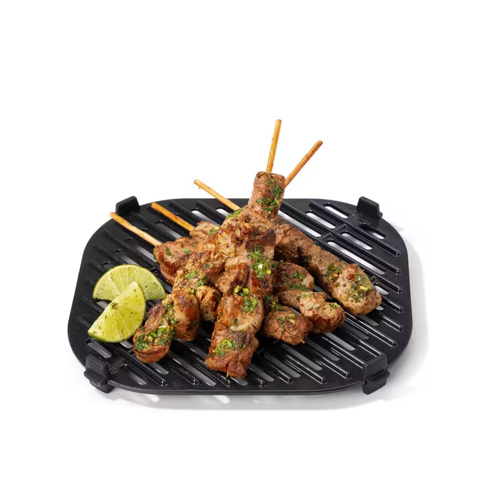 Gegrilde vleesspiesjes met groene kruiden op een zwarte grillpan, naast limoenpartjes. Witte achtergrond.