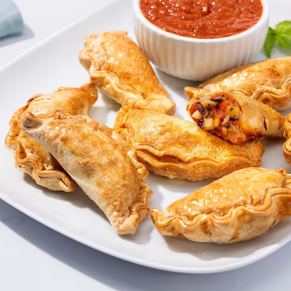 Een bord met goudbruine empanadas, een opengesneden om de vulling te laten zien. Een kleine kom rode saus.