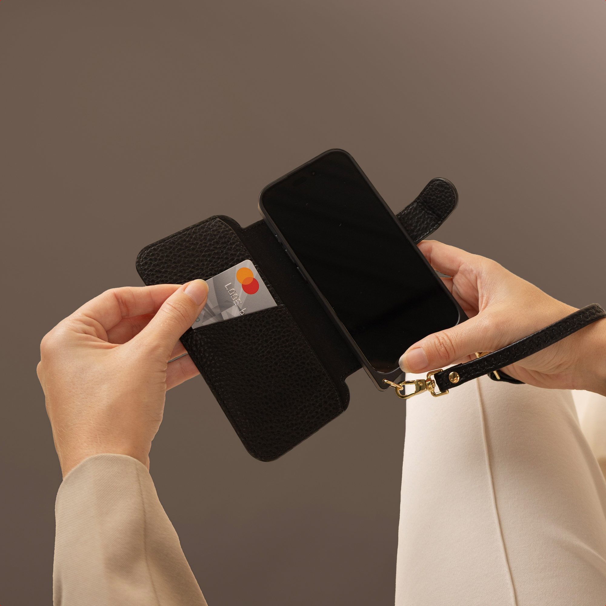 Een persoon houdt een zwarte telefoonhoes vast met een creditcard erin en een telefoon. Beige achtergrond.