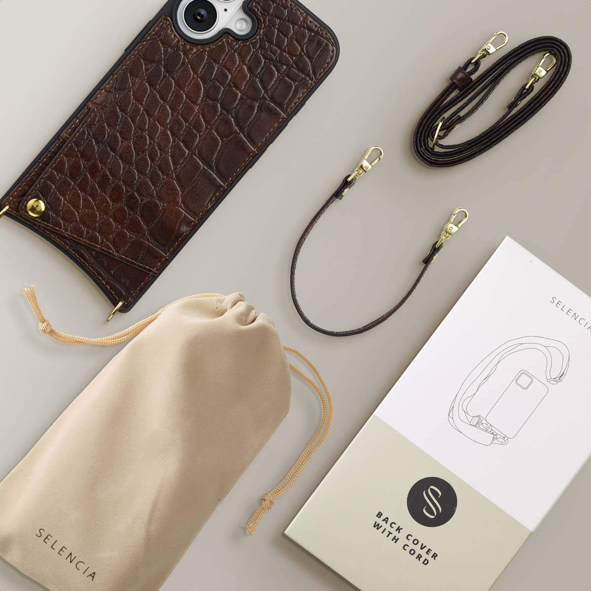 Bruine telefoonhoes, riem en etui. Een witte doos met een telefoonillustratie en de woorden 'Back cover with cord' is aanwezig.