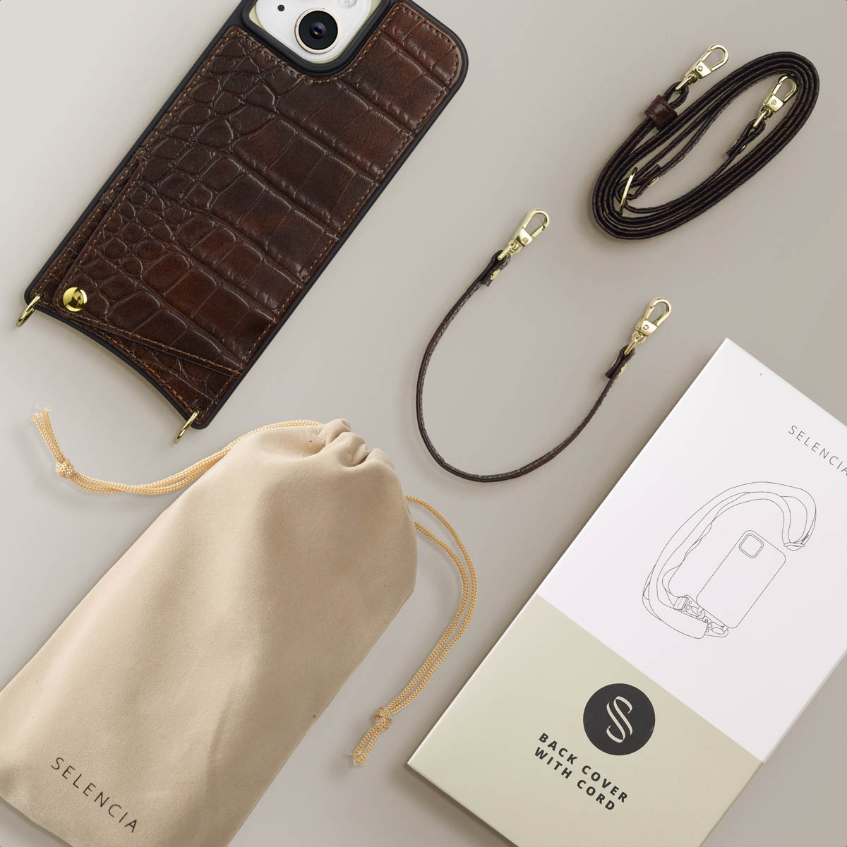 A brown leather phone case, bag, cords, and a box with a phone cover diagram on a light gray surface.