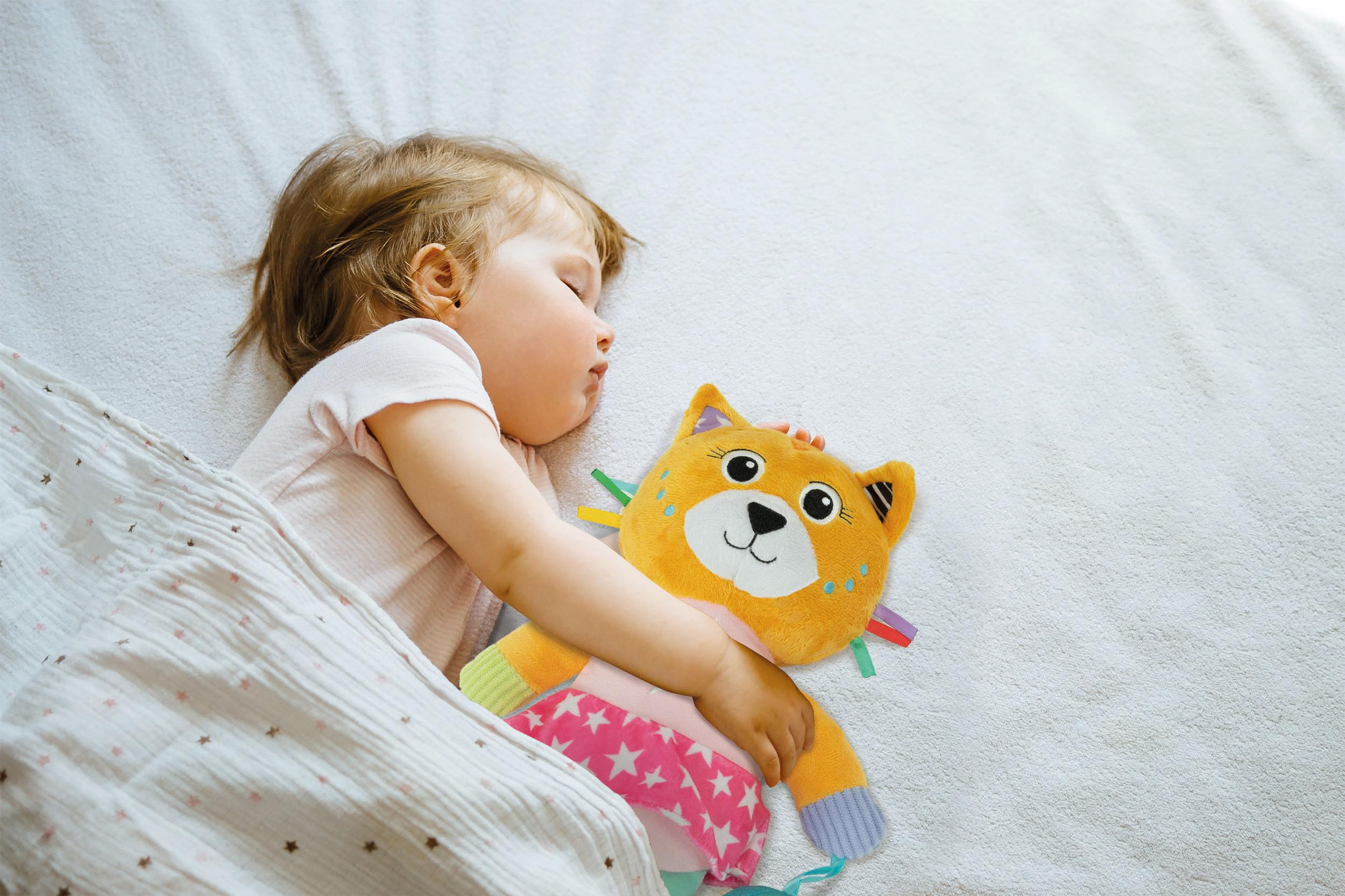 Un bambino che dorme con un gatto giocattolo. Il bambino è in un letto sotto una coperta bianca.