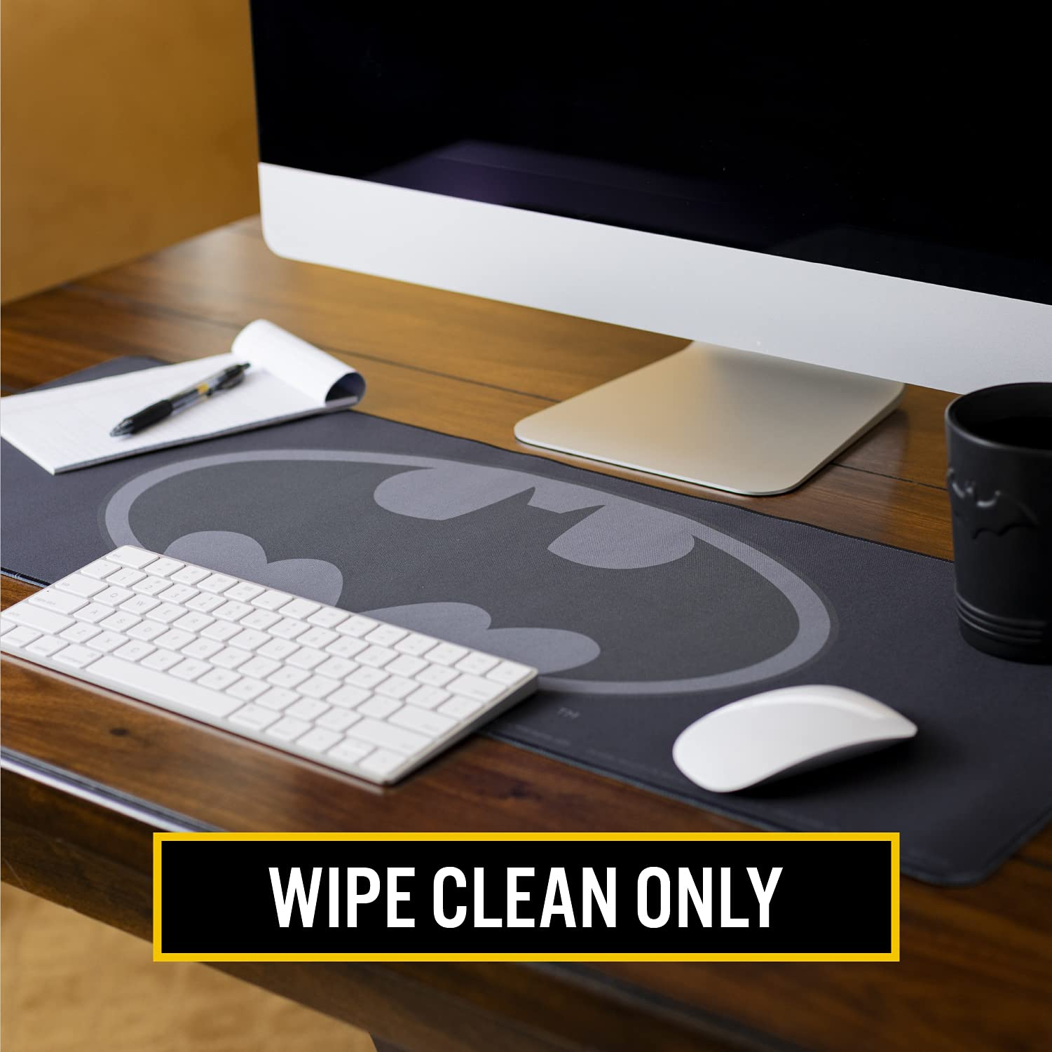 Ein Schreibtisch mit einer Batman-Mausunterlage, einem Computer, einer Tastatur, einer Maus, einem Notizblock und einer Tasse.