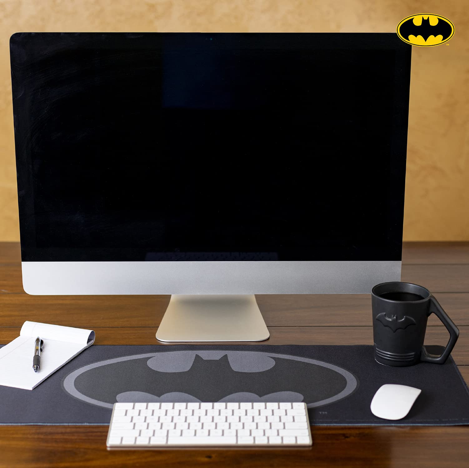 Ein Schreibtisch mit Computer, Batman-Mauspad und -Tasse, Tastatur, Notizblock und Stift. Der Hintergrund ist ein Holzschreibtisch.