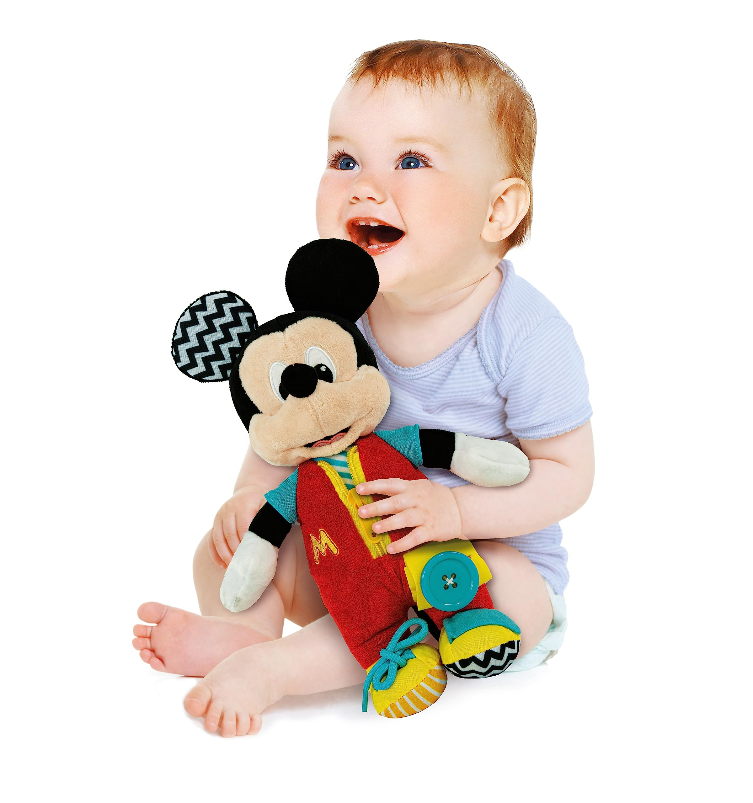 Ein Baby mit blauen Augen hält ein Mickey Mouse-Plüschtier. Das Baby lächelt und blickt nach oben. Weißer Hintergrund.