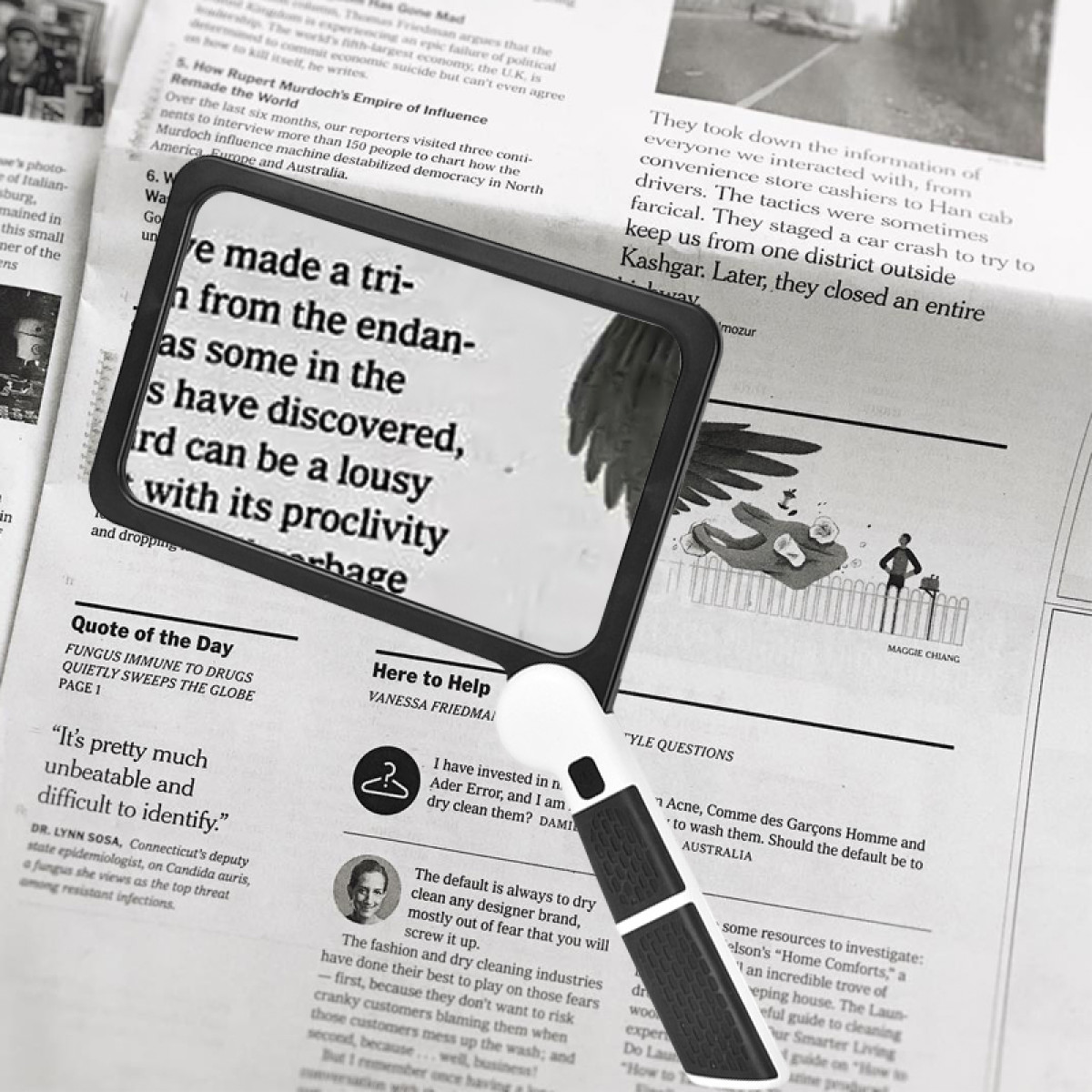 Lupa nad tekstem gazety. Widoczne nagłówki i artykuły. Czarno-biały obraz.