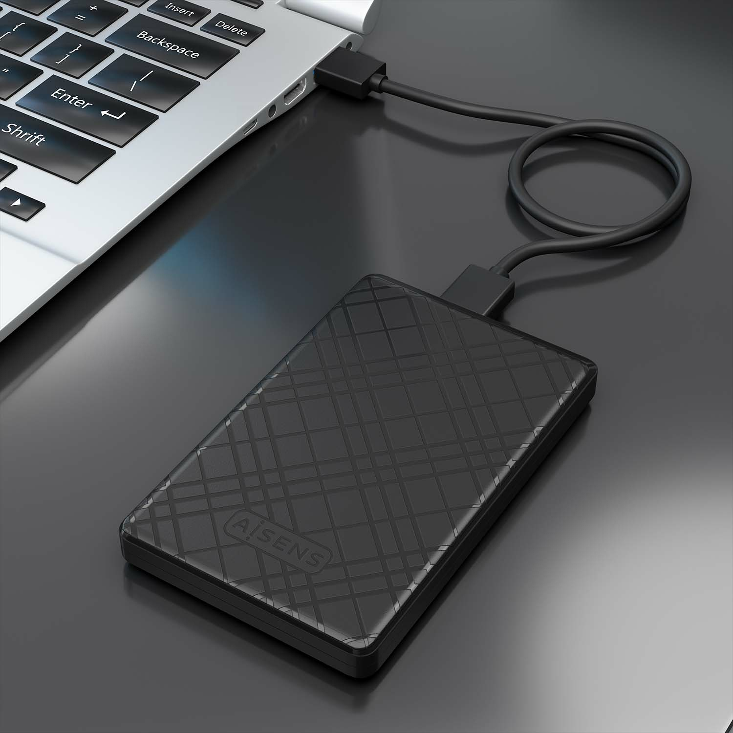 Un disco duro externo negro conectado a un portátil. El disco está sobre una superficie reflectante.