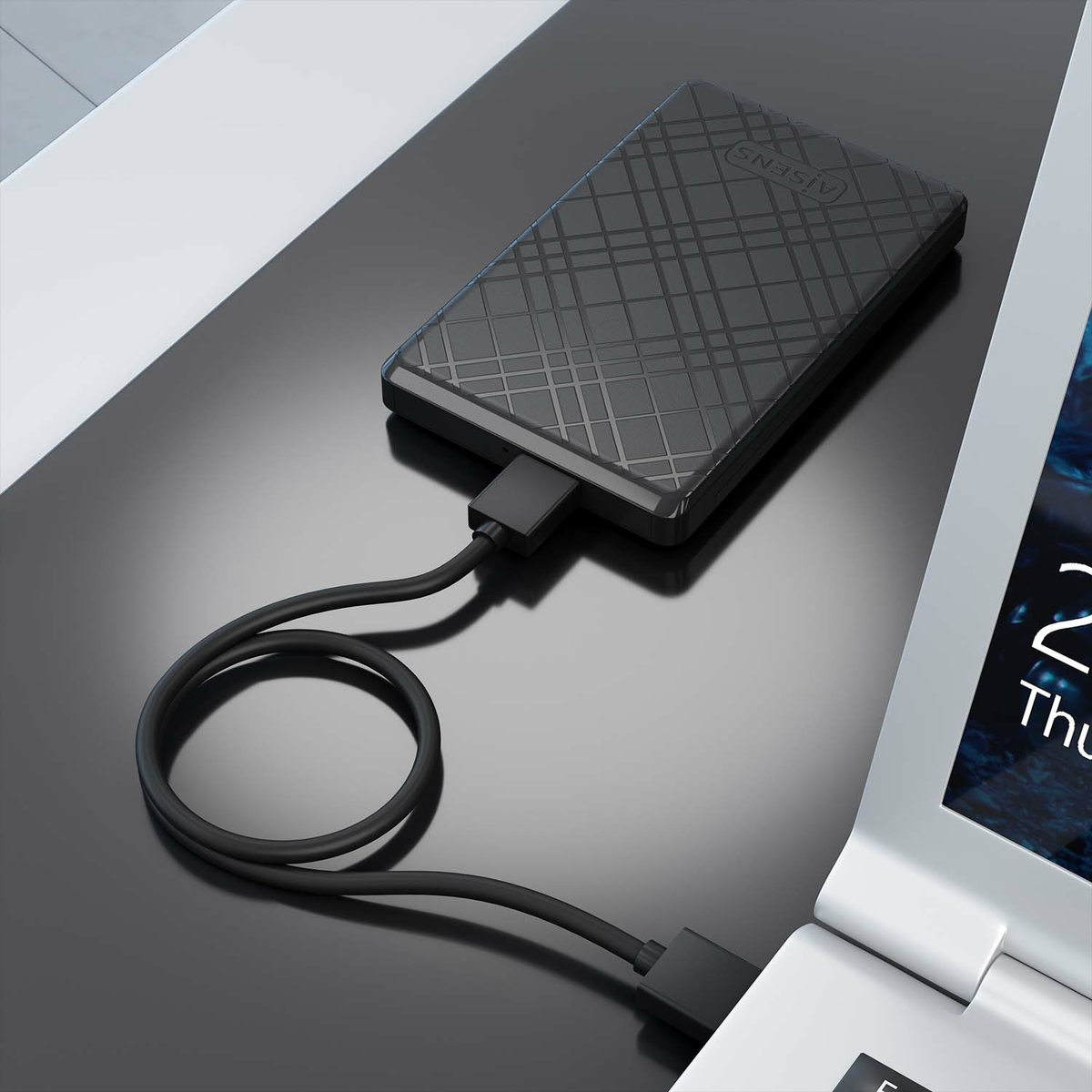 Un disco duro externo negro con un cable conectado a una laptop. El disco está en una superficie negra reflectante.