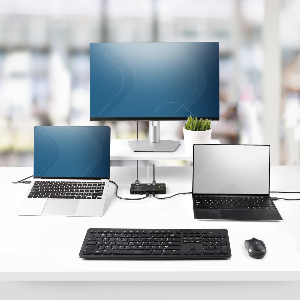 Una configuración de escritorio con dos portátiles, un monitor, teclado, ratón y una estación de acoplamiento. Todo en un escritorio blanco.