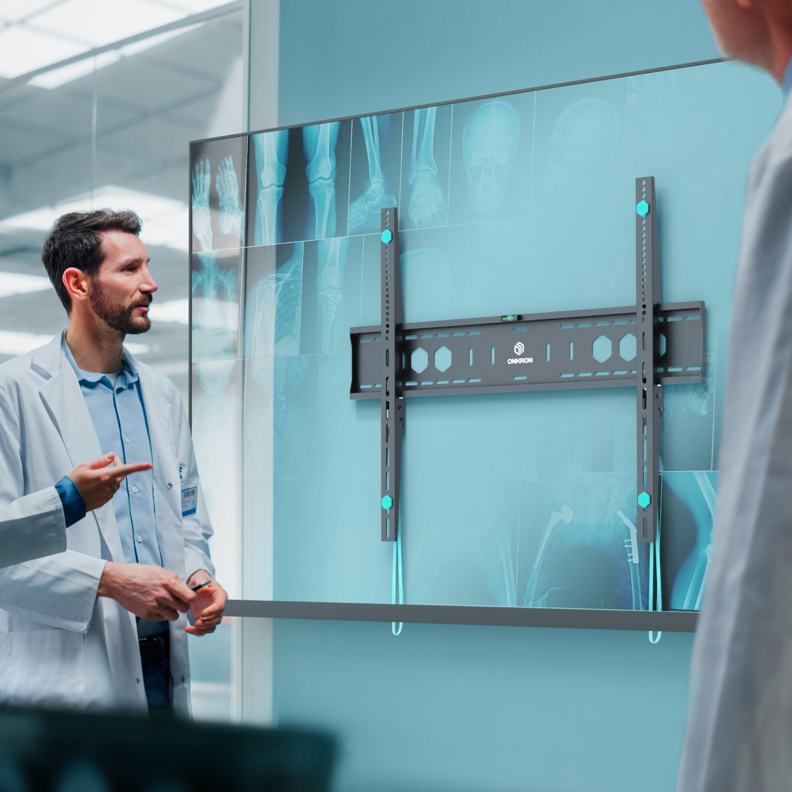 Dwóch lekarzy w białych fartuchach omawia zdjęcia rentgenowskie na ścianie. Widoczny jest uchwyt do telewizora. Scena rozgrywa się w otoczeniu medycznym.