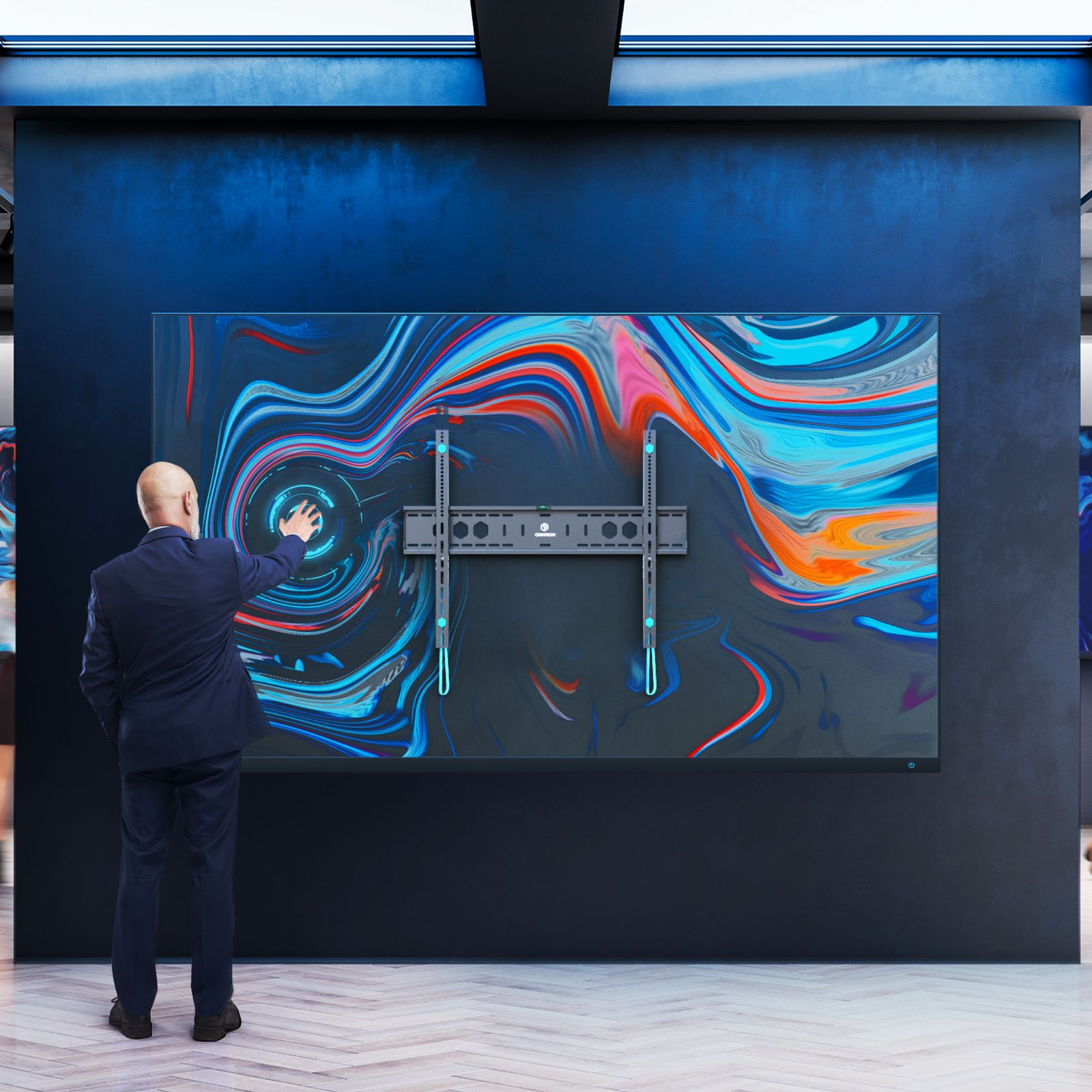 Mężczyzna w garniturze wskazuje na duży ekran z kolorową sztuką abstrakcyjną i uchwytem do telewizora.
