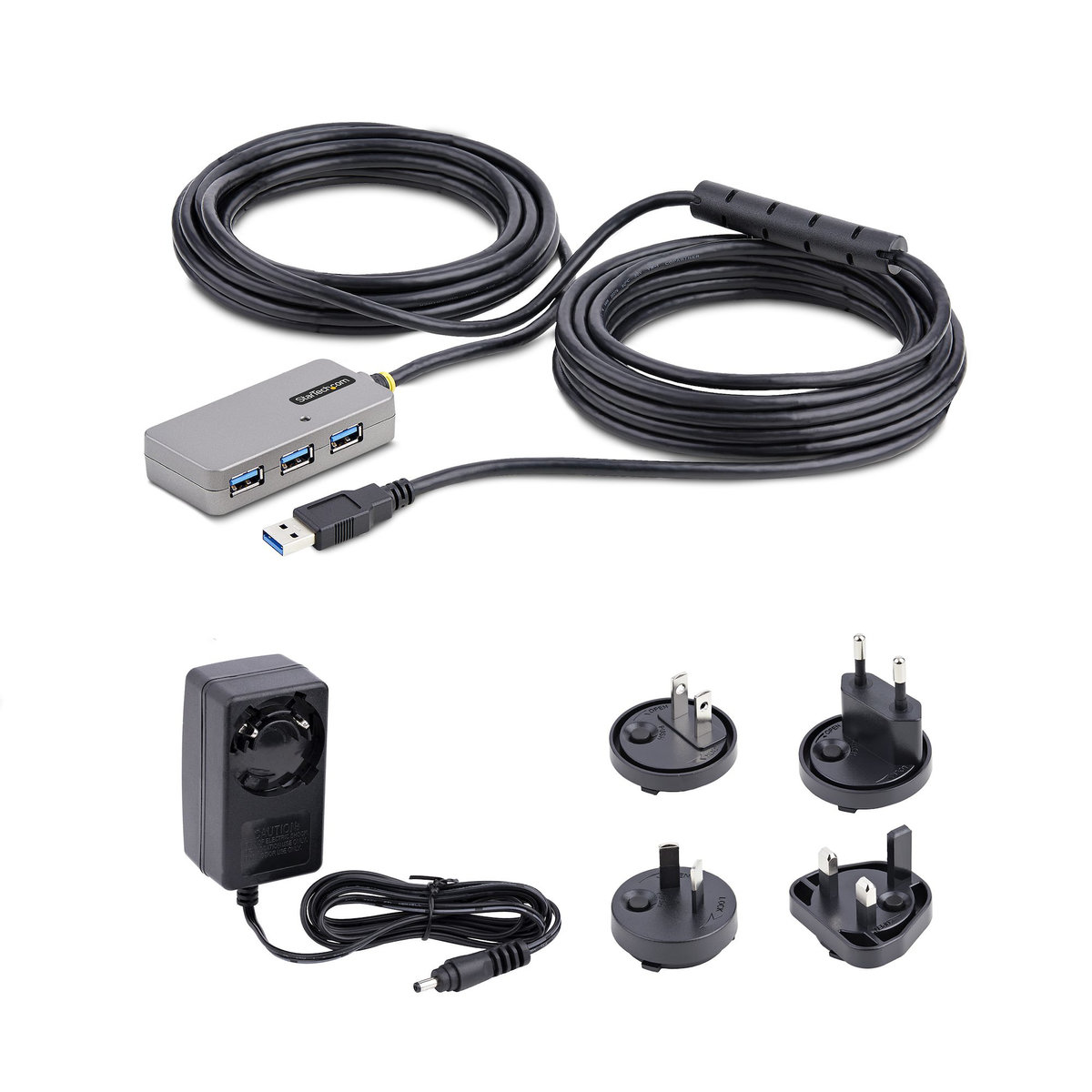 Un concentrador USB, un adaptador de corriente y varios adaptadores de enchufe se muestran sobre una superficie blanca. El concentrador es gris, los cables son negros.