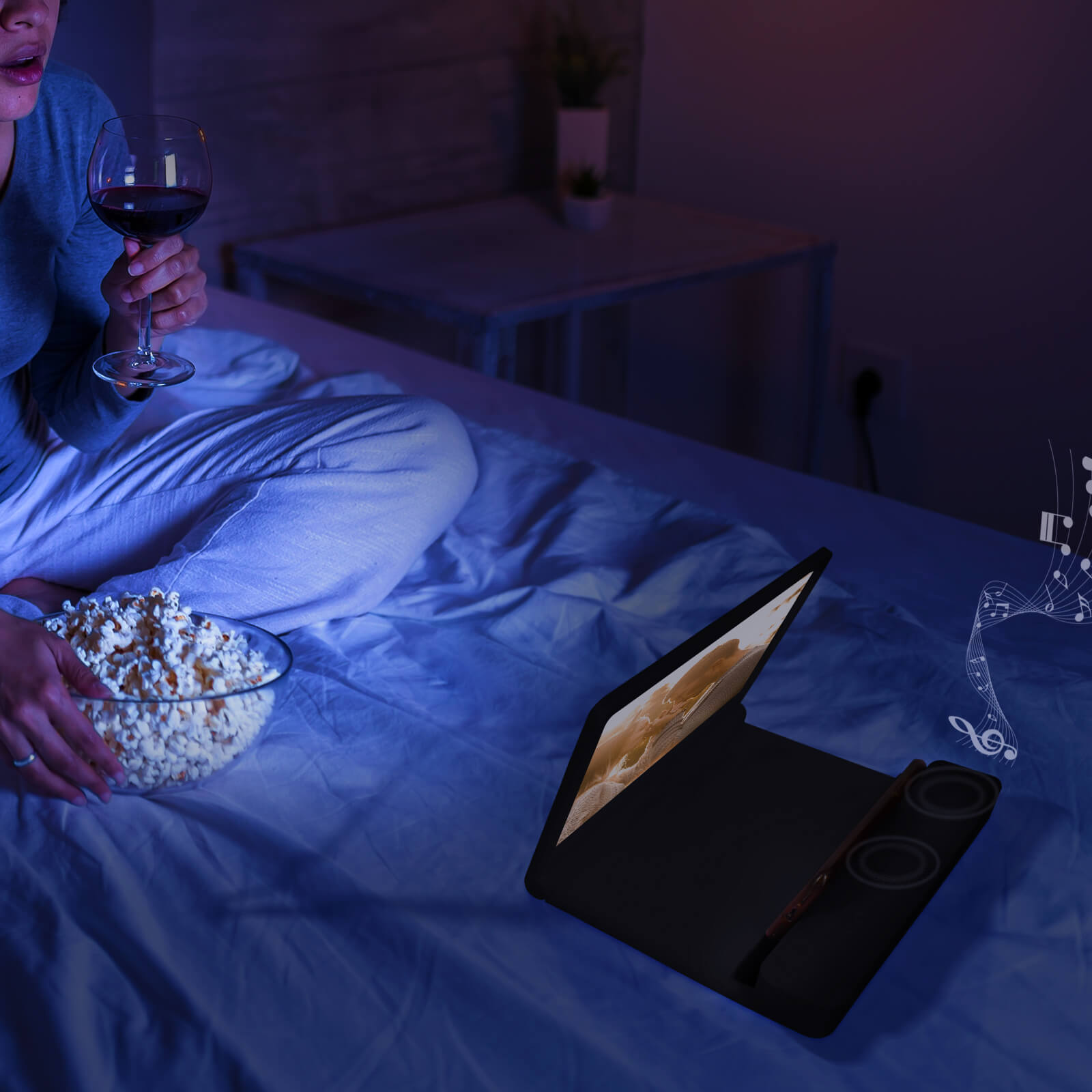 Una persona en la cama, viendo una película en una computadora portátil, con palomitas de maíz y vino. La escena es oscura y acogedora.