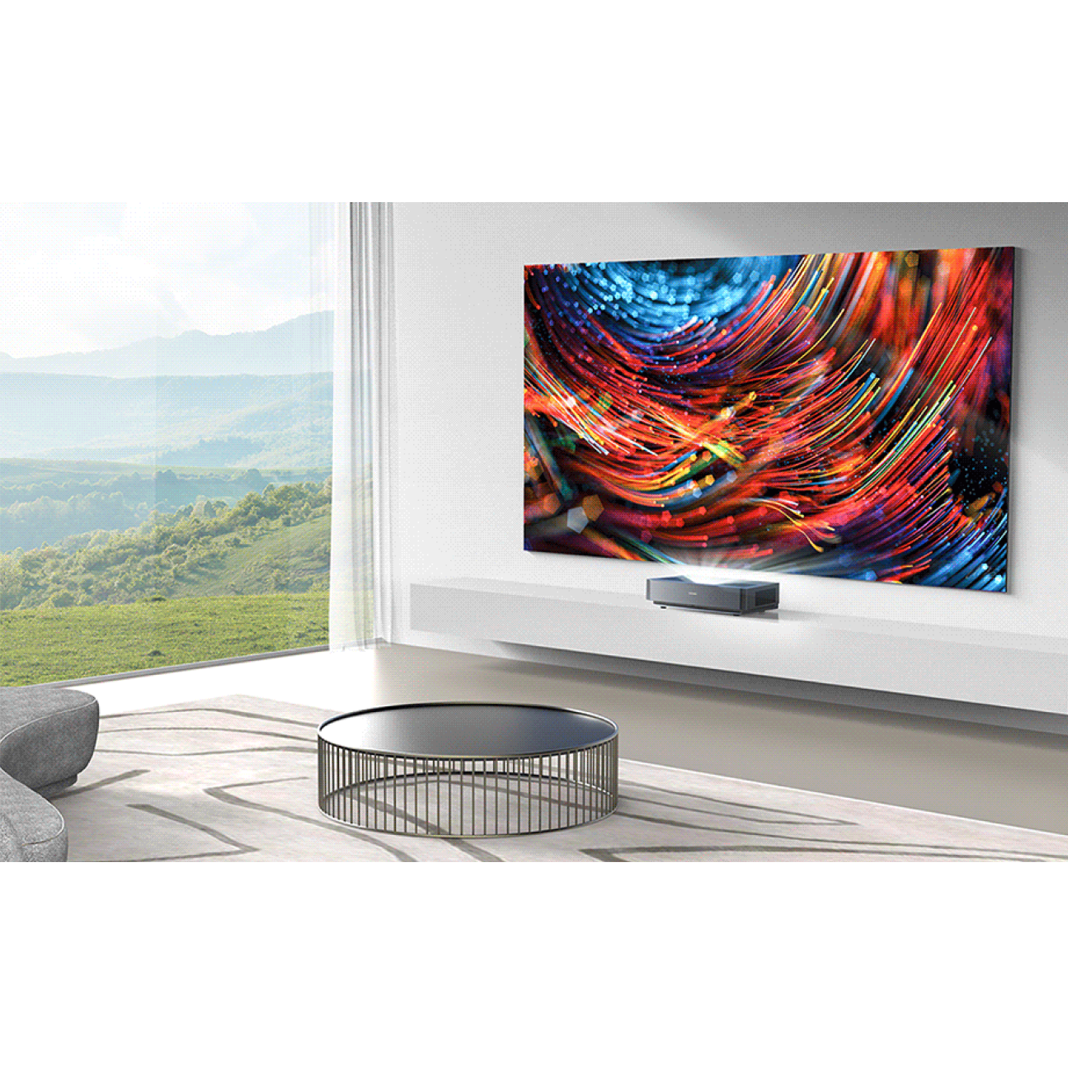 Nowoczesny salon z dużym ekranem wyświetlającym kolorową sztukę. Poniżej projektor. Na zewnątrz zielony krajobraz.