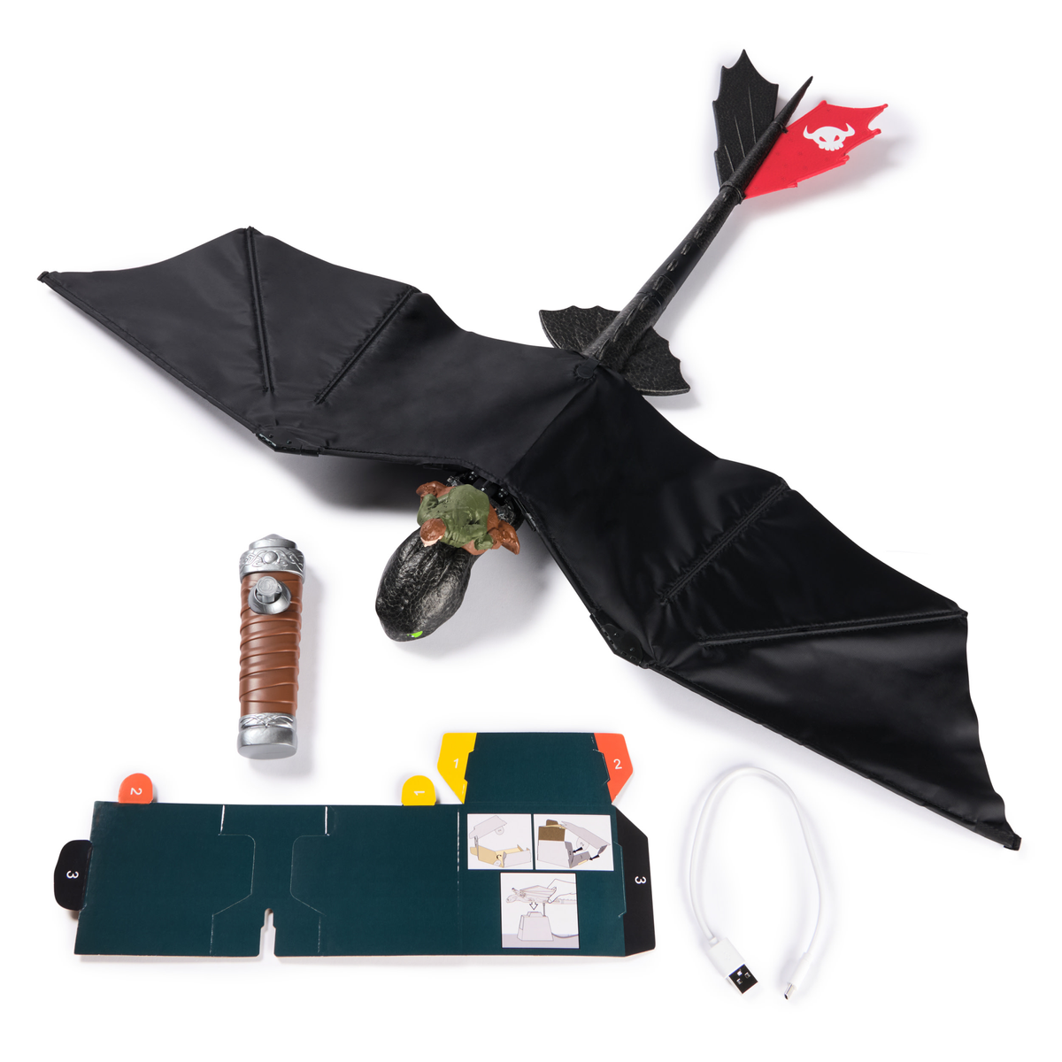 Un dragón de juguete con alas negras, un mango marrón, un cable de carga y una hoja de instrucciones de cartón sobre blanco.
