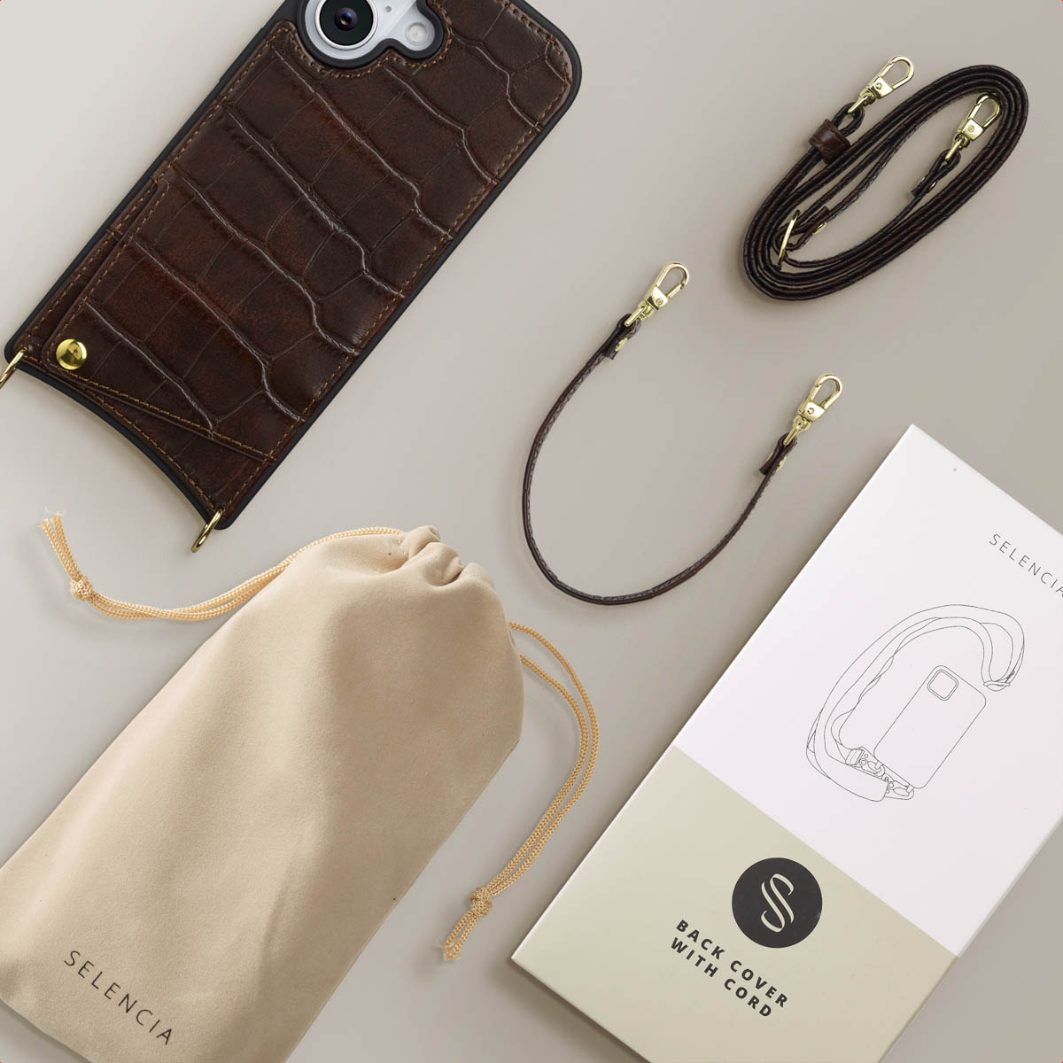 Een telefoonhoesje, tas en koordset. De hoes is bruin met een krokodillenpatroon. Accessoires liggen op een lichtgrijze ondergrond.