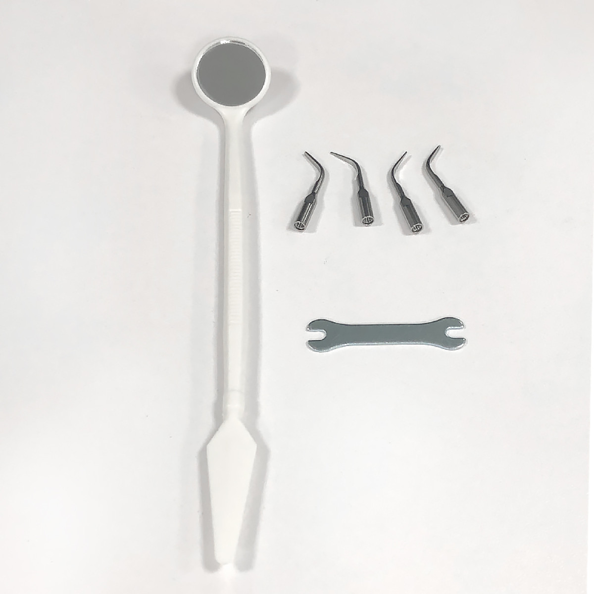 Narzędzia dentystyczne na białym tle. Zawiera lusterko, cztery kątowe metalowe końcówki i klucz. Wszystkie narzędzia są ułożone na białej powierzchni.
