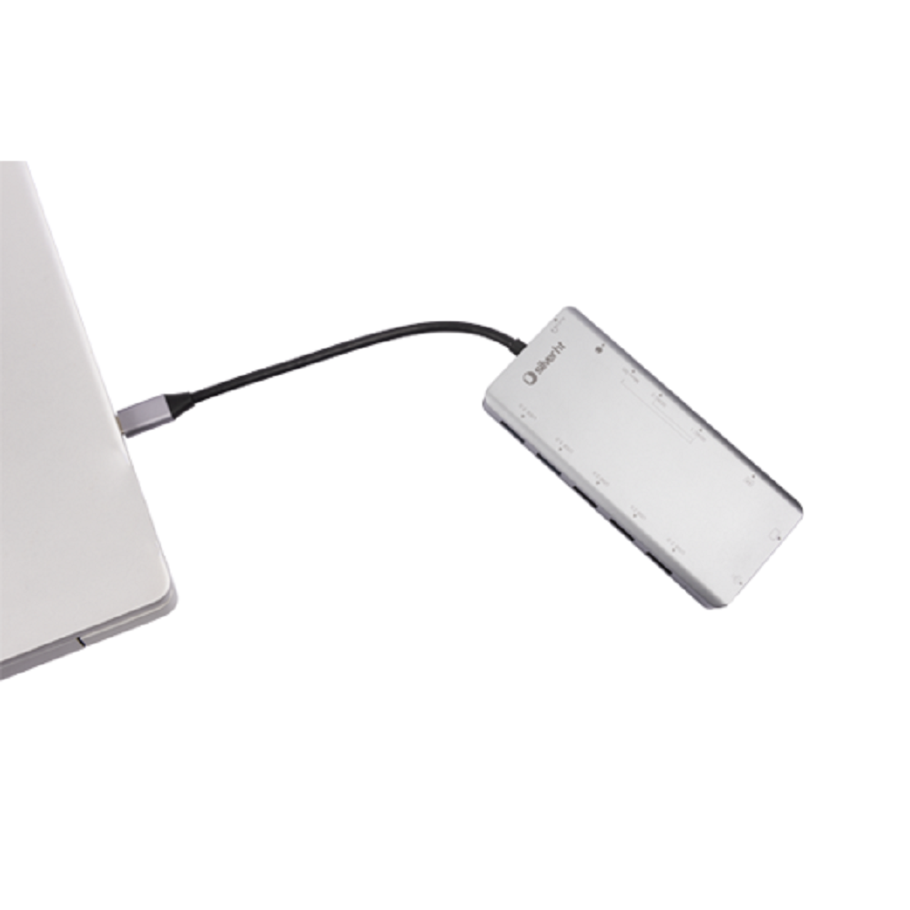 Un hub USB argentato collegato a un laptop con un cavo nero. L'hub è angolato e ha più porte. Lo sfondo è bianco.