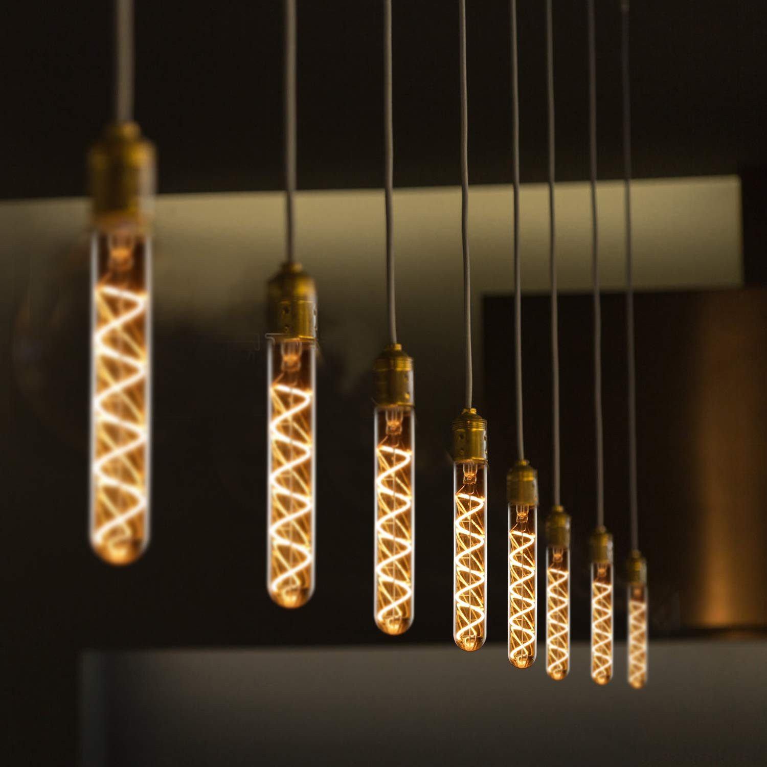 Nove lampadine appese e luminose con un filamento a spirale caldo. Sono appese a fili su uno sfondo scuro, in fila.