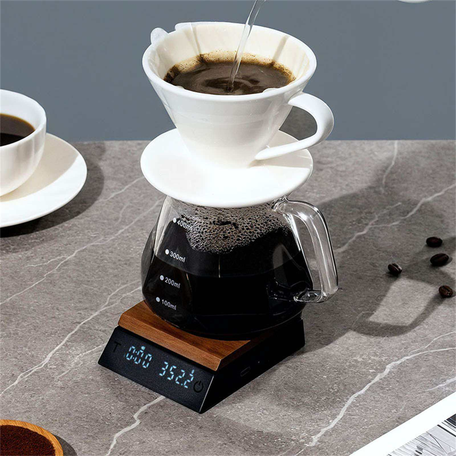 Kaffee wird gebrüht. Ein weißer Filter sitzt auf einer Glaskaraffe auf einer Waage. Eine weitere Tasse ist im Hintergrund.