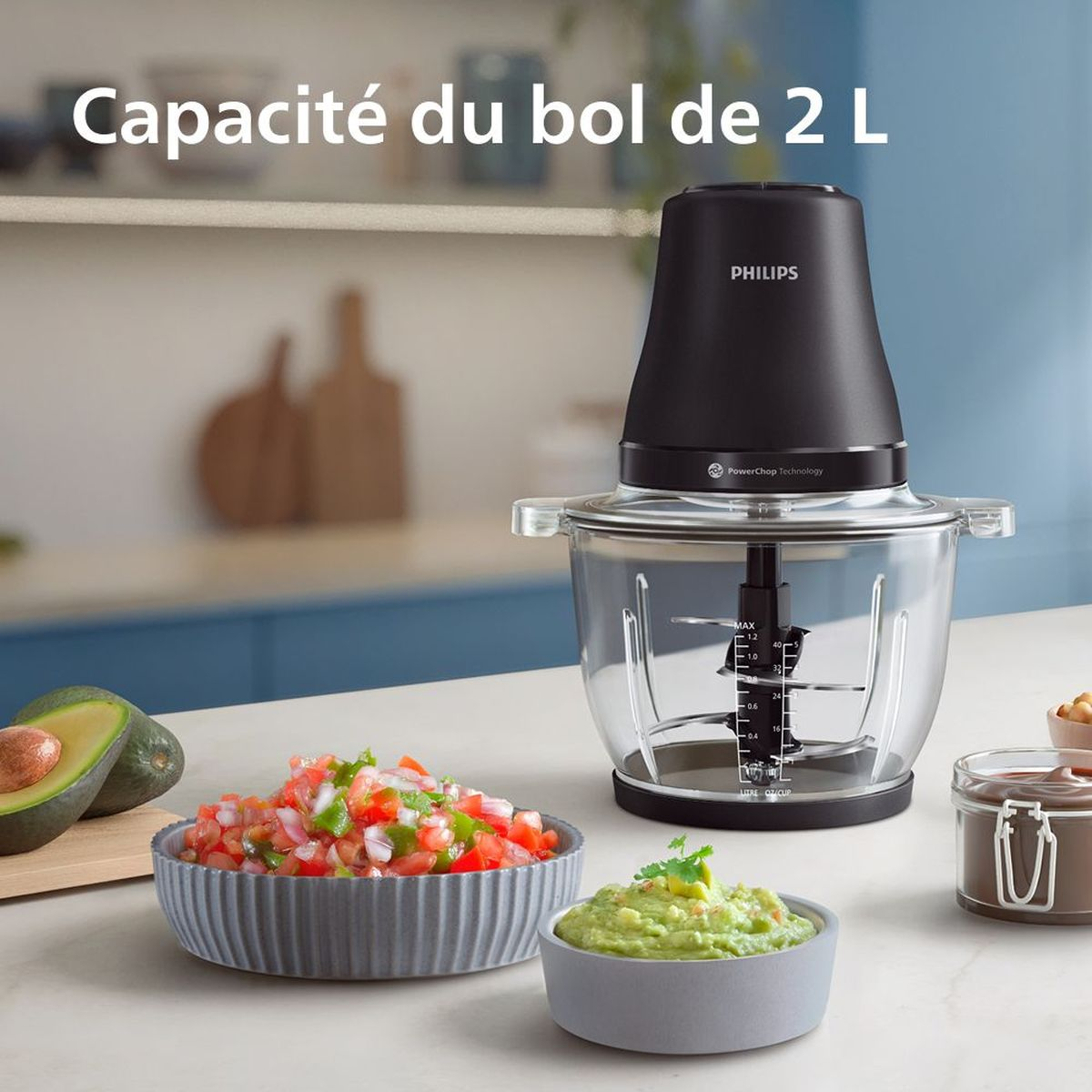 Ein Philips-Küchengerät mit Glasschüssel. Schalen mit Salsa, Guacamole und Avocado sind davor. Der Hintergrund umfasst ein Schneidebrett.