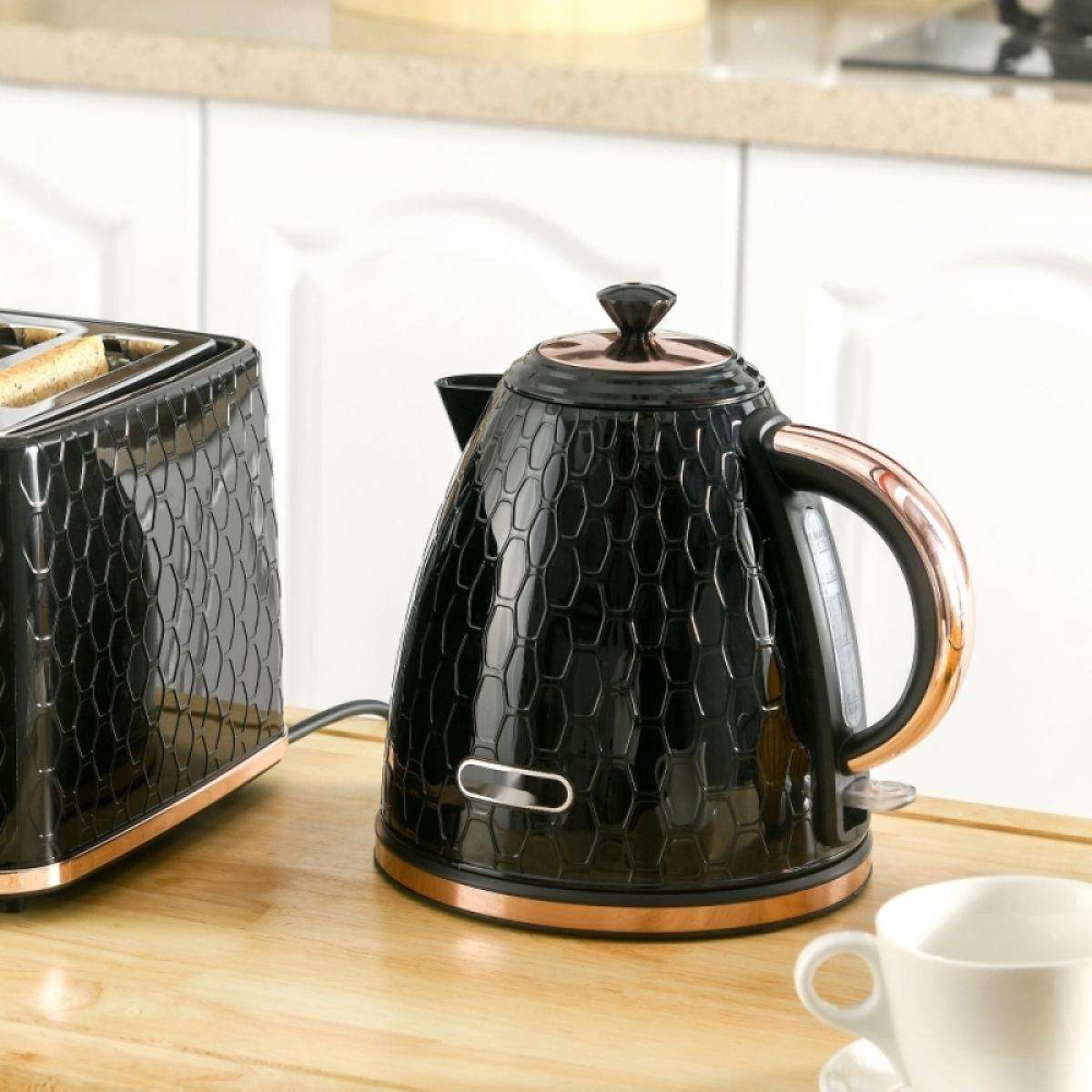 Ein schwarzer Wasserkocher und Toaster mit kupferfarbenen Akzenten stehen auf einer Holzoberfläche. Eine weiße Tasse ist im Vordergrund, im Hintergrund ein weißer Schrank.