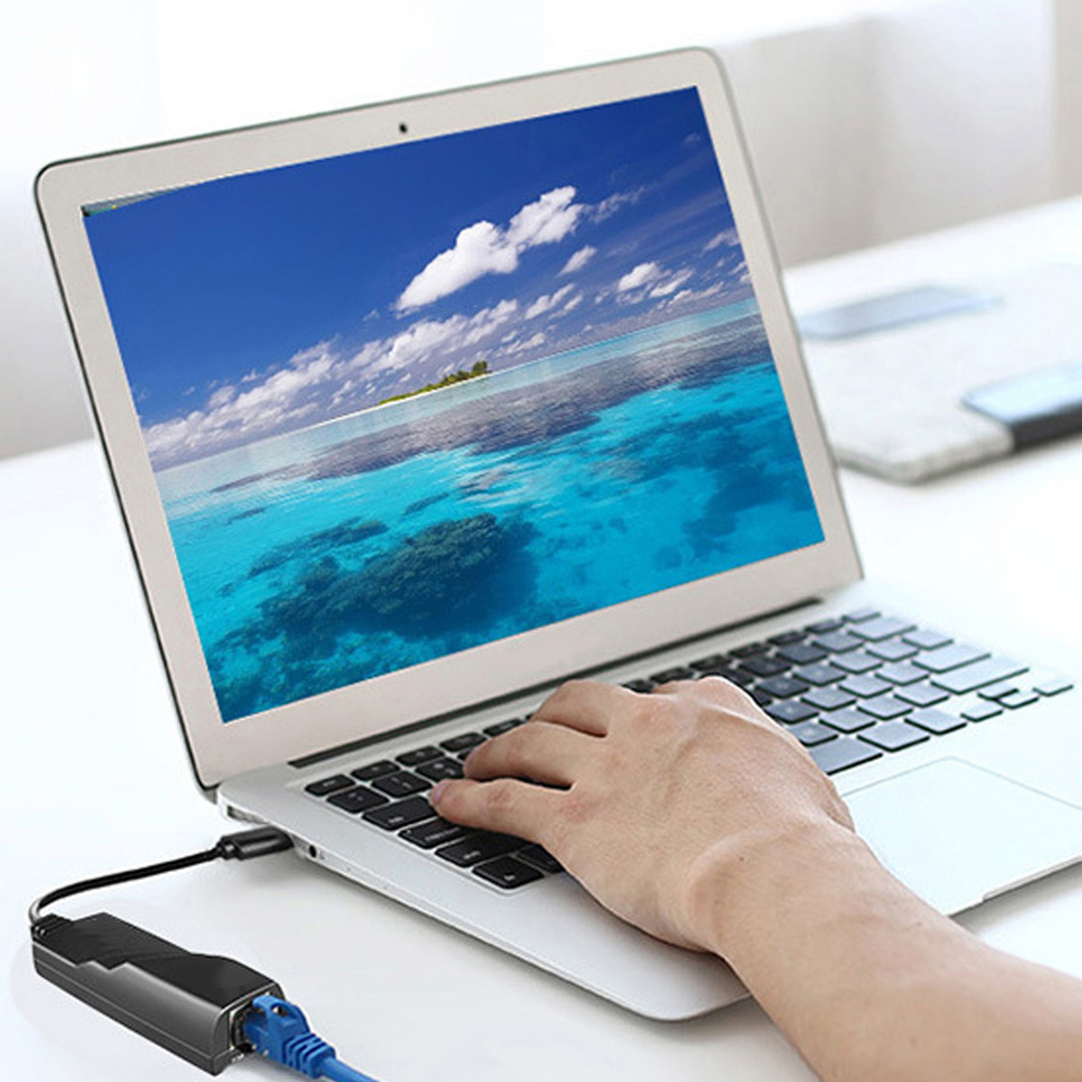 Laptop mit tropischer Strandszene. Eine Hand tippt auf der Tastatur. Netzwerkkabel ist am Laptop angeschlossen.
