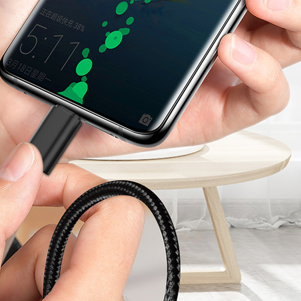 Eine Hand, die ein Telefon hält und es mit einem schwarzen Kabel auflädt. Der Bildschirm zeigt Zeit und Ladestatus.