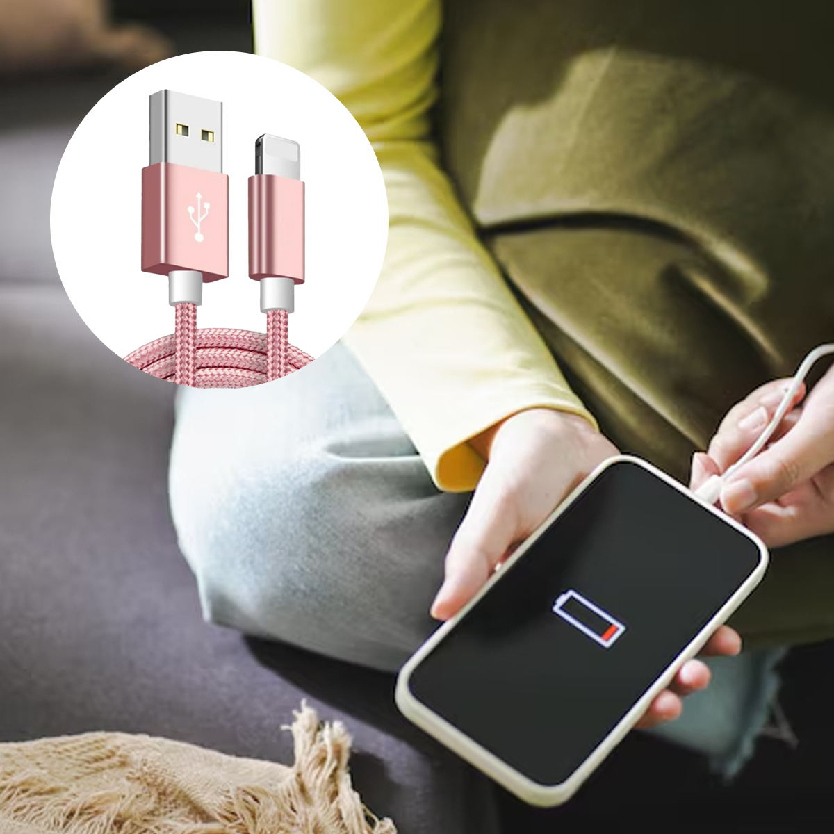 Eine Person lädt ein Smartphone mit einem rosa Ladekabel auf. Der Akku des Telefons ist leer. Im Hintergrund sind Sofa und Kleidung.