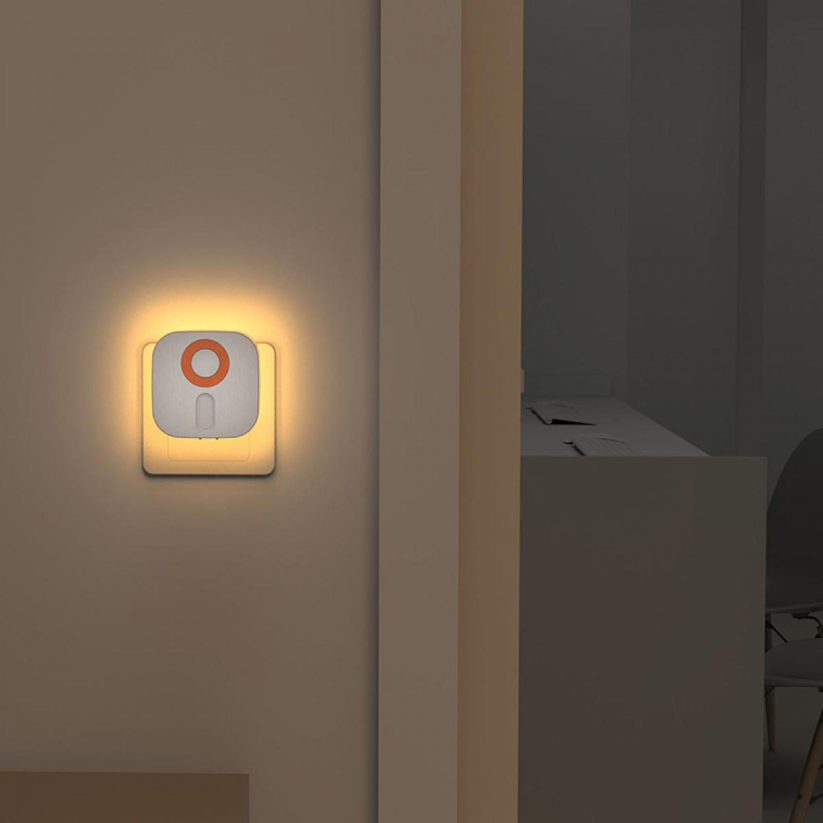 Ein Nachtlicht mit rotem Kreis an der Wand. Ein Türrahmen führt zu einem dunklen Raum mit Schreibtisch und Stuhl.