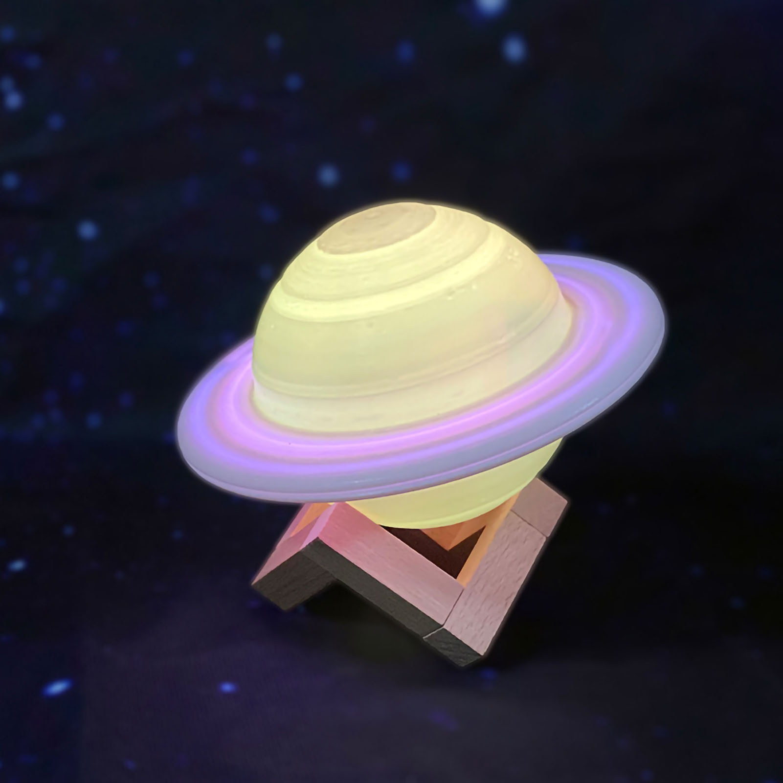 Eine leuchtende Saturnlampe mit hellgelbem Körper und lila Ring auf einem Holzständer vor sternenklarem Hintergrund.