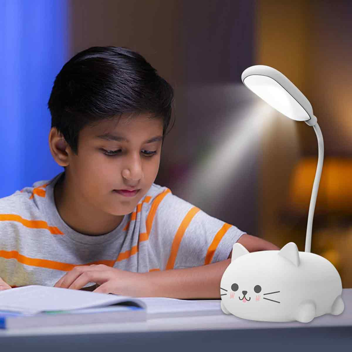 Ein Junge lernt unter einer katzenförmigen Lampe. Er trägt ein gestreiftes Hemd. Ein Notizbuch liegt offen auf dem Schreibtisch.