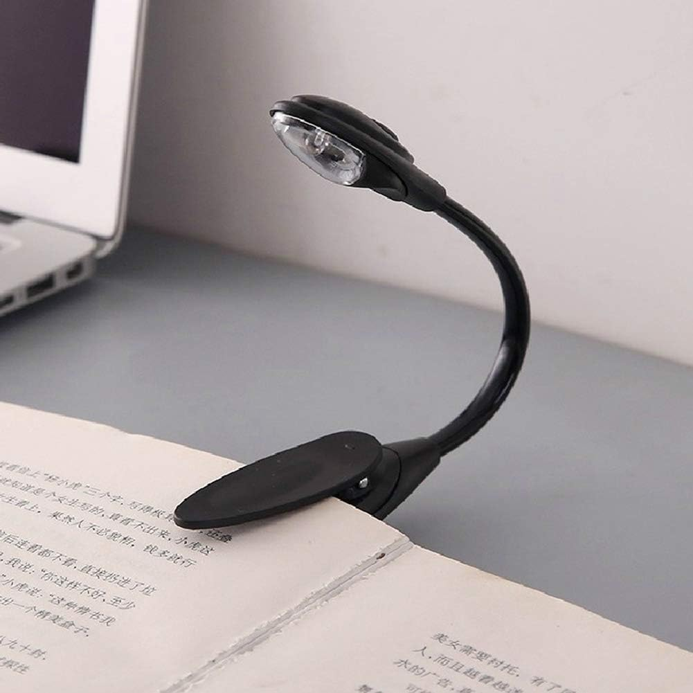 Eine schwarze LED-Buchleuchte ist an einem Buch befestigt. Im Hintergrund ist ein Laptop zu sehen. Das Licht ist an.