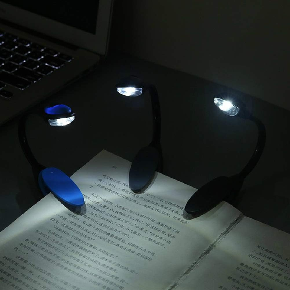 Drei Buchlampen beleuchten ein Buch auf einem Tisch. Im Hintergrund ist ein Laptop zu sehen.