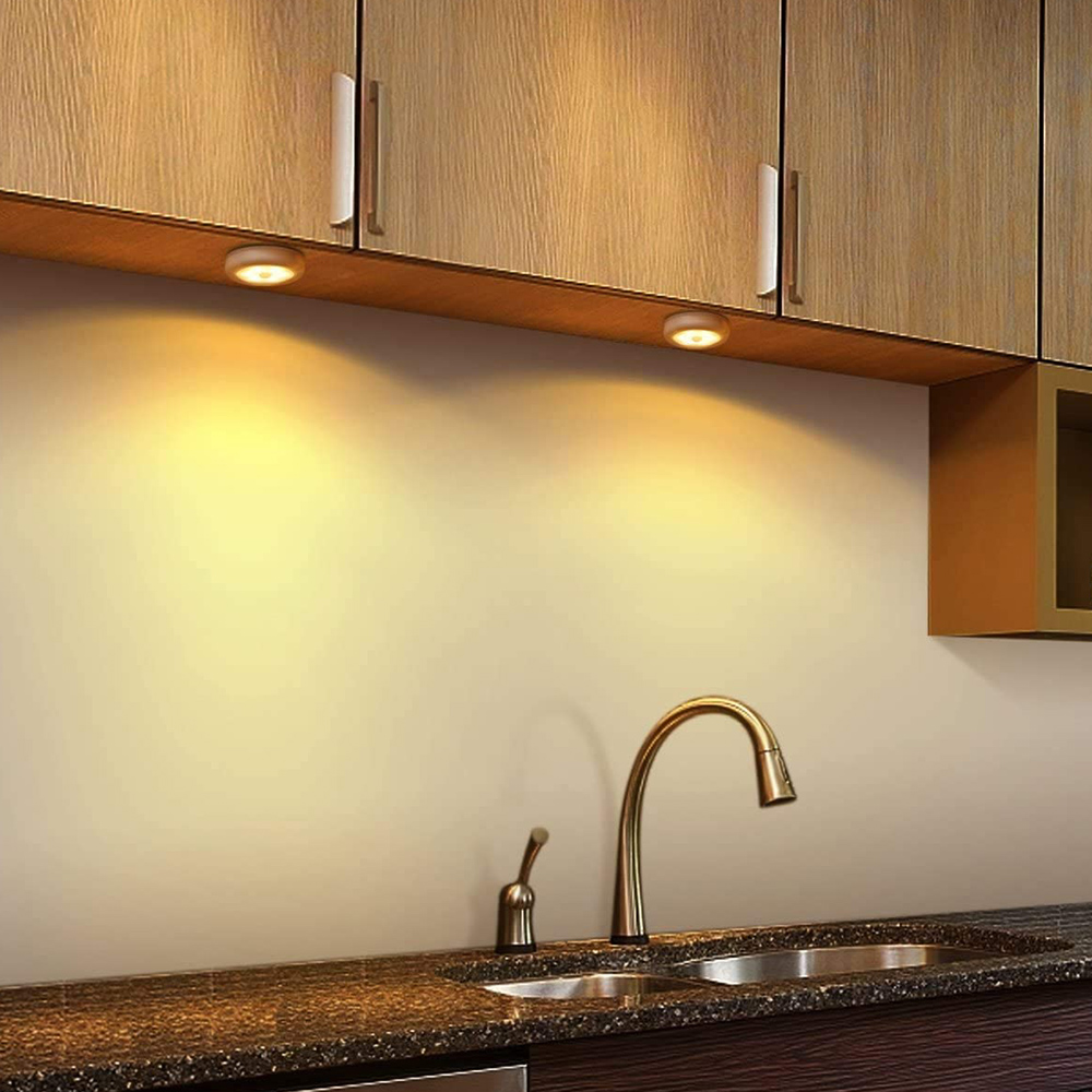 Eine Küchenszene mit Holzschränken, einem Waschbecken und einem Wasserhahn. Zwei Lichter beleuchten die Arbeitsplatte. Die Szene ist gut beleuchtet.