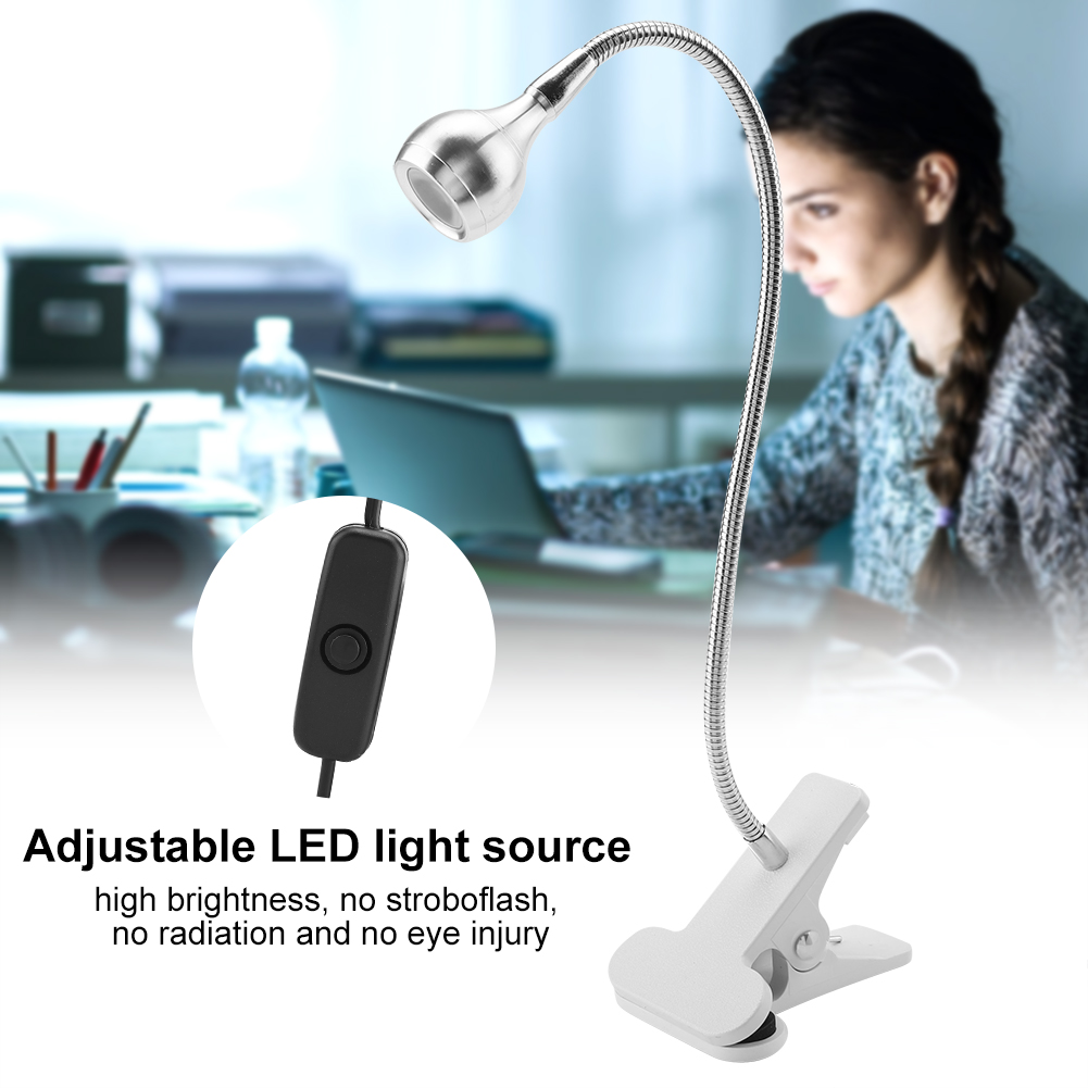 Eine flexible LED-Lampe mit Clip steht auf einem Tisch. Im Hintergrund arbeitet eine Frau an ihrem Laptop. Ein Netzschalter ist ebenfalls sichtbar.