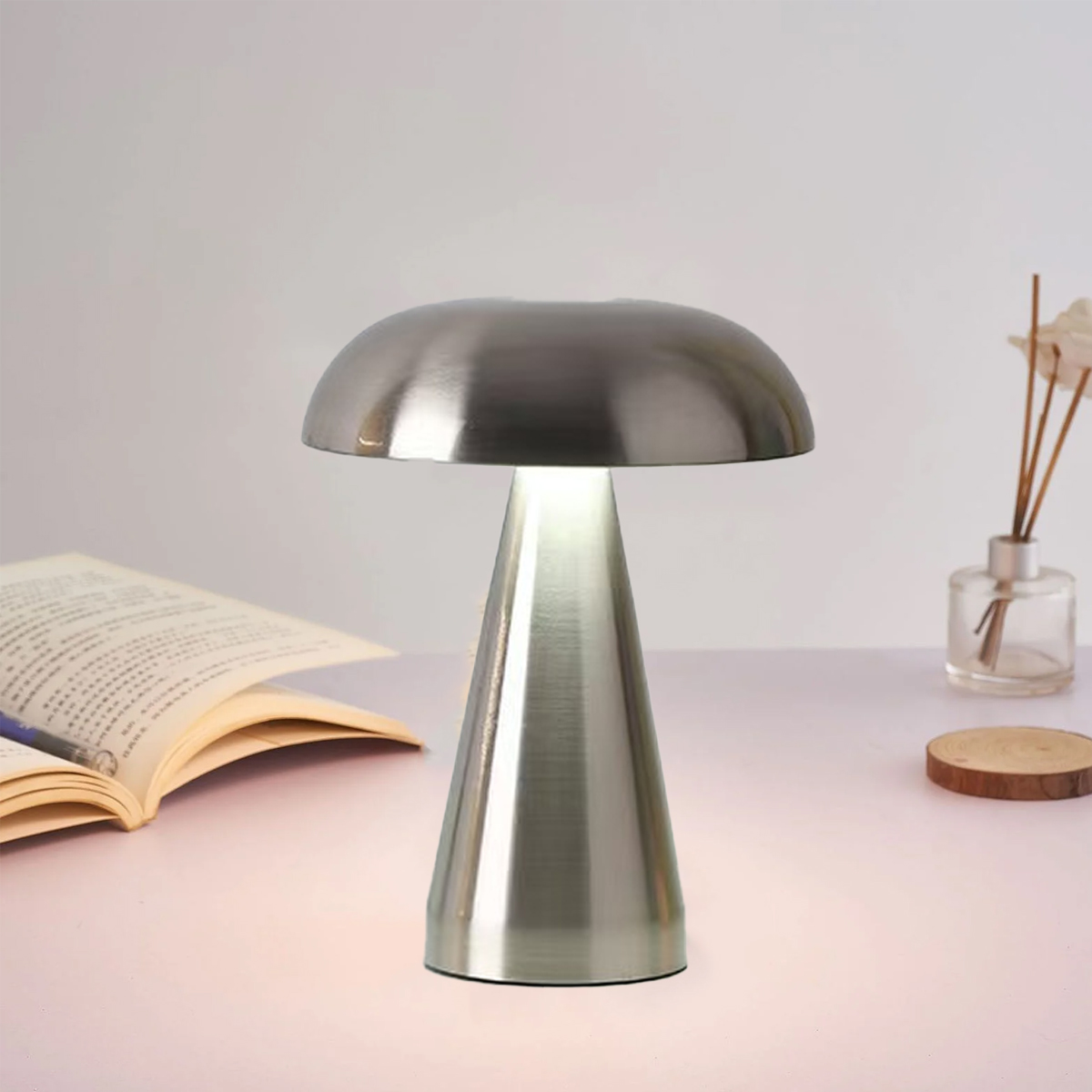 Eine metallische Tischlampe mit pilzförmigem Oberteil und konischem Sockel steht auf einem weißen Tisch. Ein offenes Buch und eine kleine Vase sind ebenfalls vorhanden.