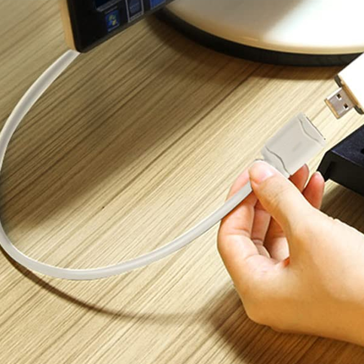 Eine Hand hält einen weißen USB-Adapter. Ein weißes Kabel verbindet einen Monitor und ein USB-Gerät.