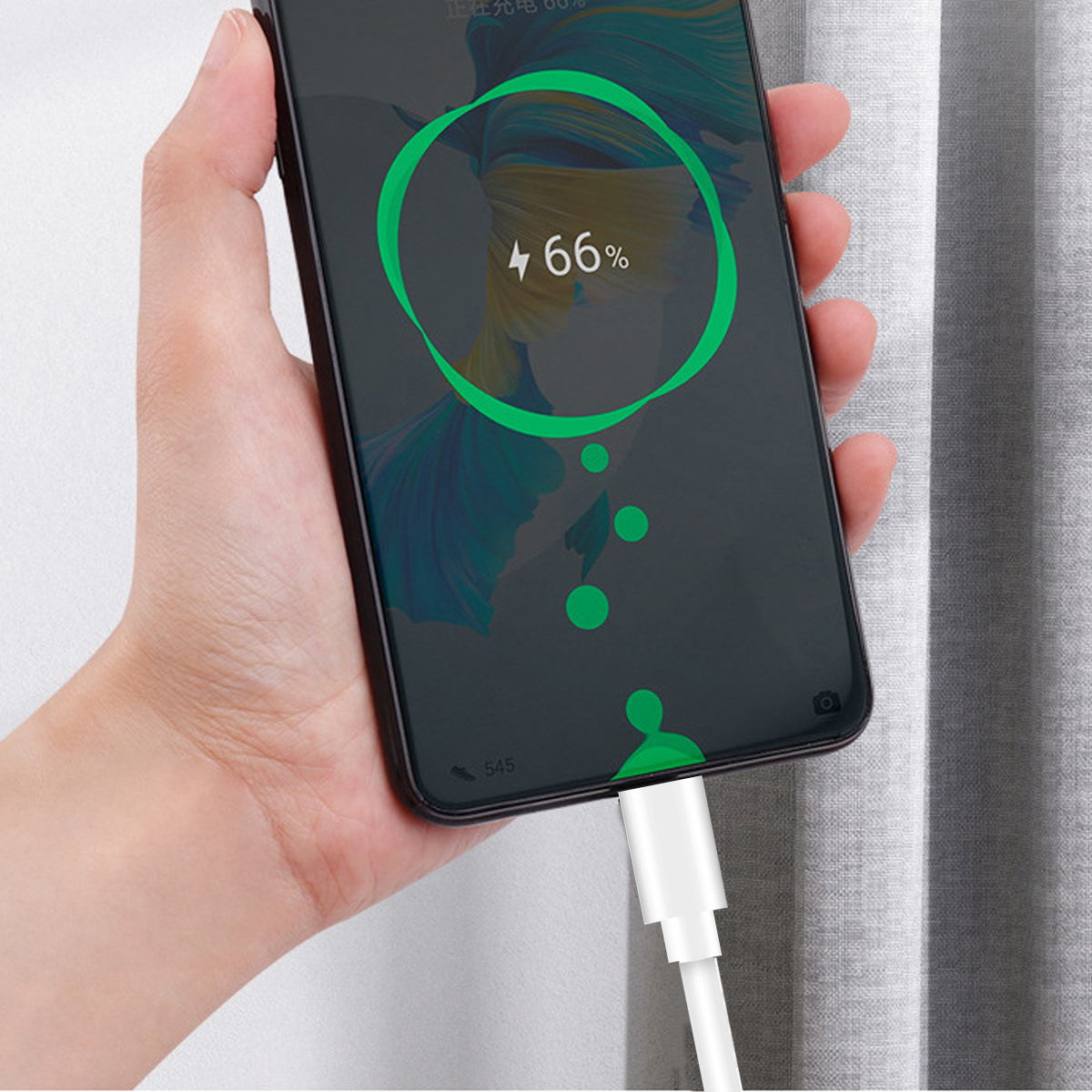 Hand hält ein Smartphone, das geladen wird. Der Bildschirm zeigt 66 % geladen an. Ein weißes Ladekabel ist eingesteckt. Hintergrund: grauer Vorhang.
