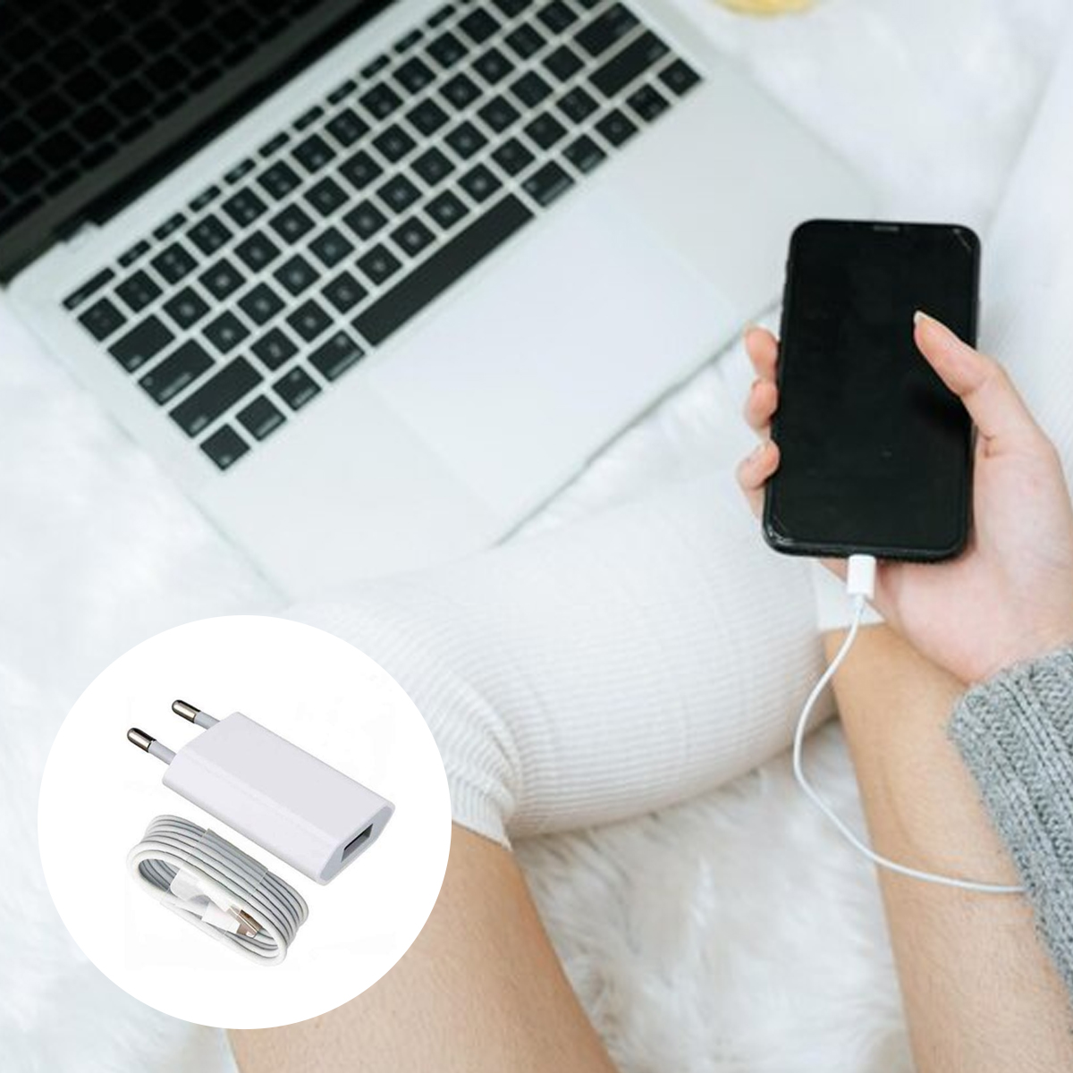 Eine Person hält ein schwarzes Smartphone, das an ein Ladegerät angeschlossen ist. Ein Laptop befindet sich im Hintergrund. Links ist ein weißes Ladegerät.