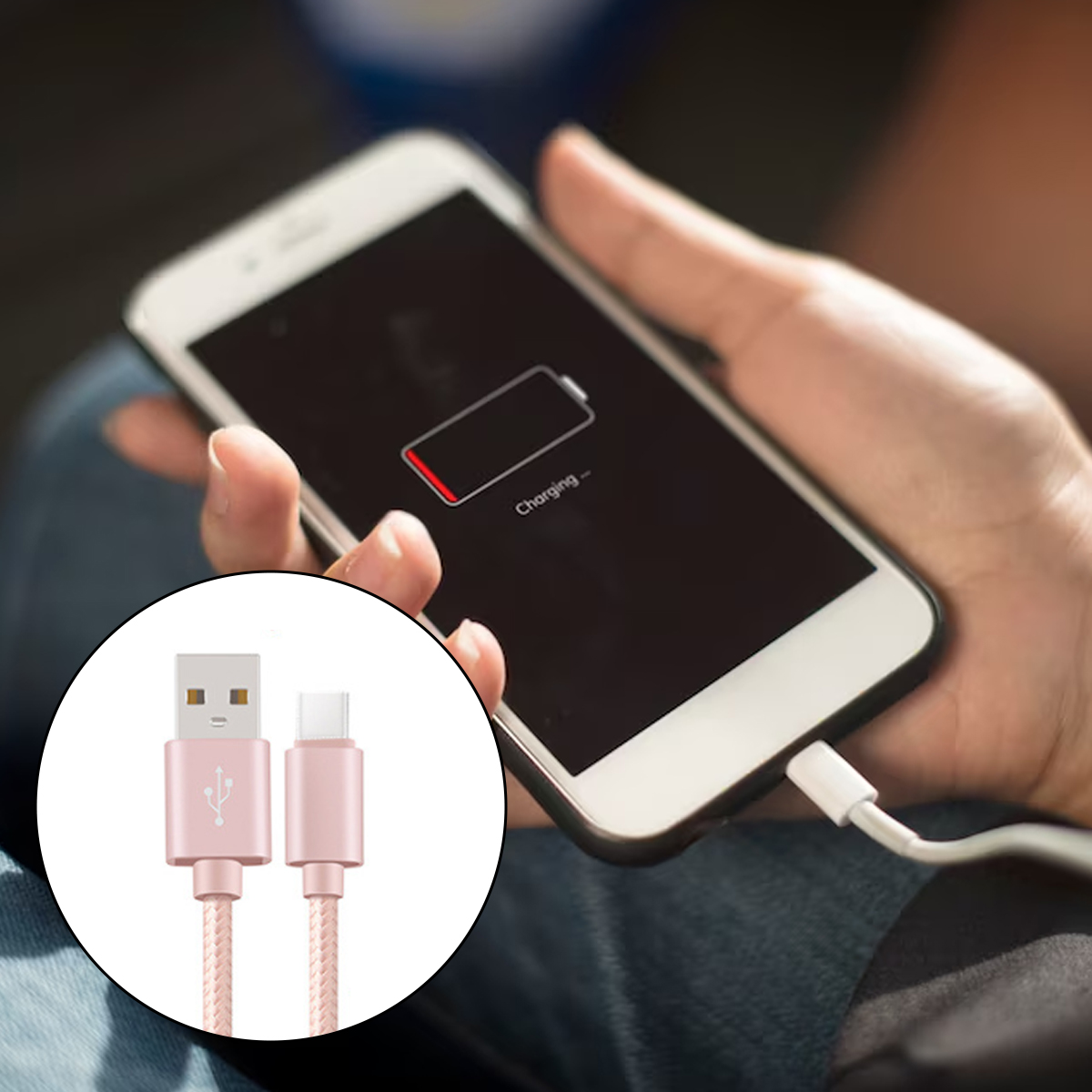 Eine Hand hält ein Telefon, das aufgeladen wird. Der Bildschirm zeigt einen niedrigen Akkustand. Ein rosa USB-Kabel ist im Vordergrund.