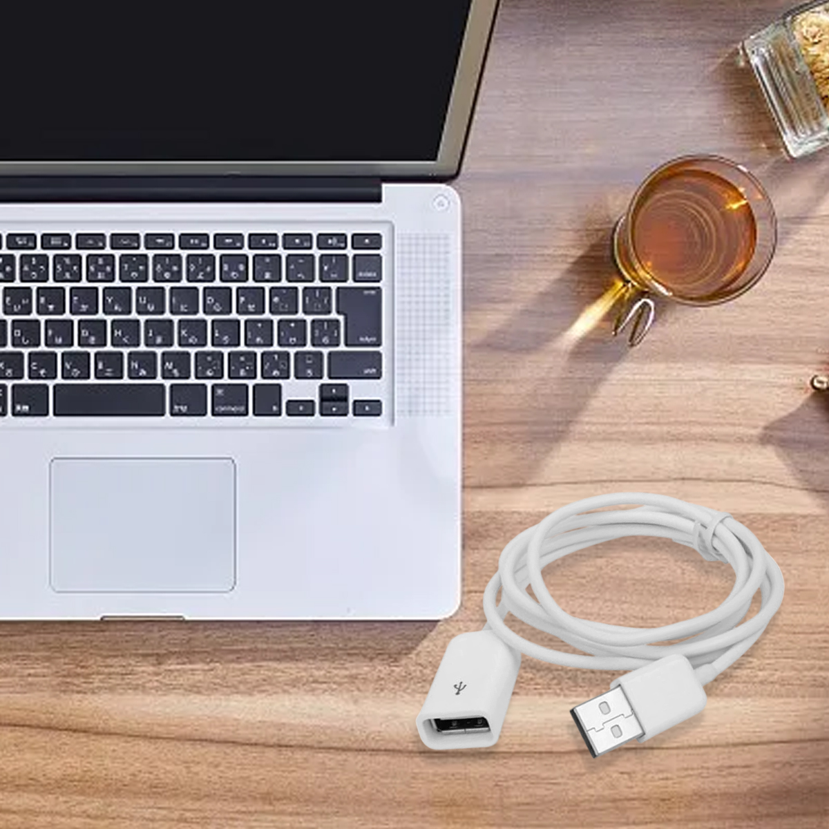 Auf einem Holztisch liegen ein Laptop, eine Tasse Tee und ein weißes USB-Kabel. Das Kabel ist neben dem Laptop aufgerollt.