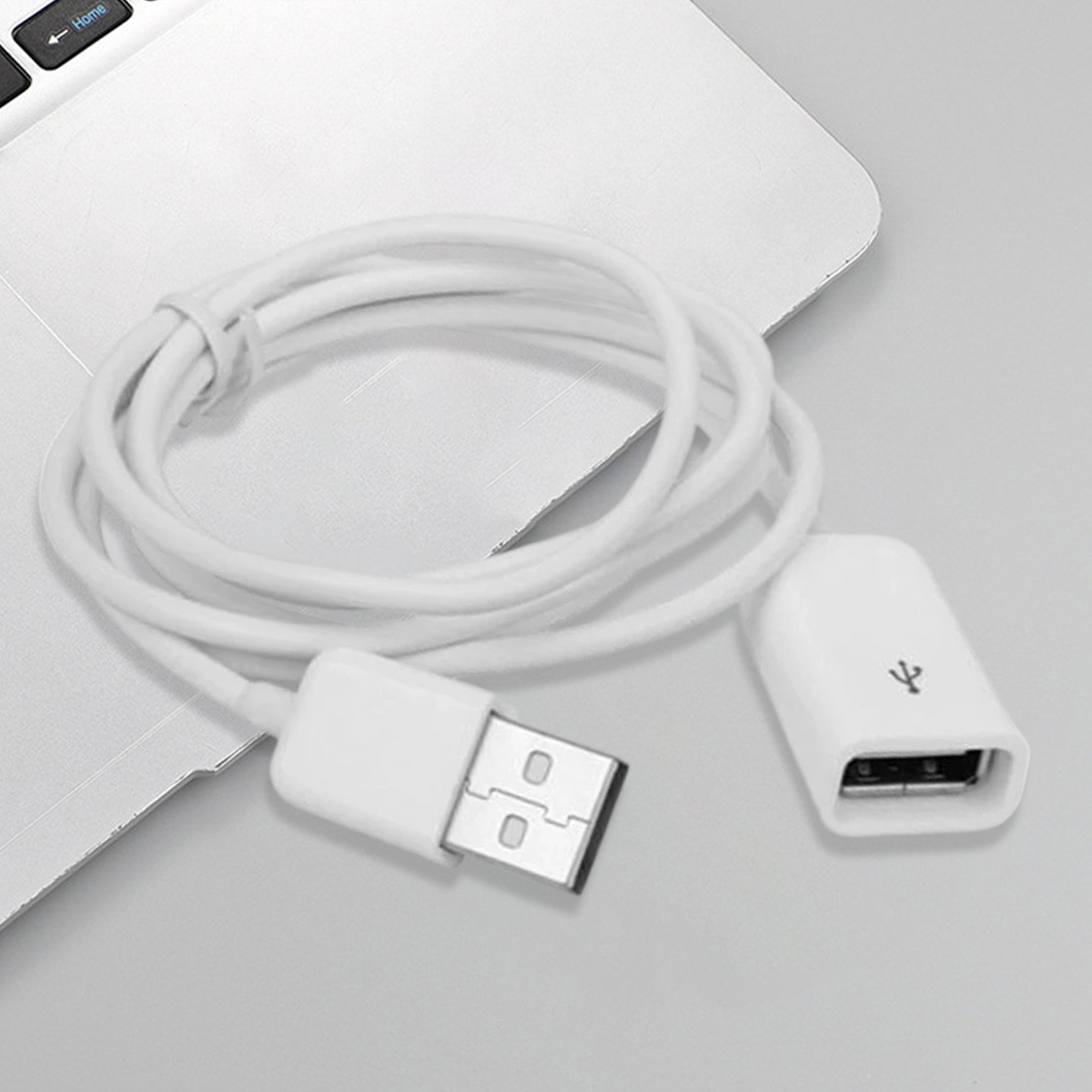 Ein weißes USB-Kabel und ein Stecker liegen auf einem silbernen Laptop. Das Kabel ist aufgerollt. Der Stecker hat ein USB-Symbol.