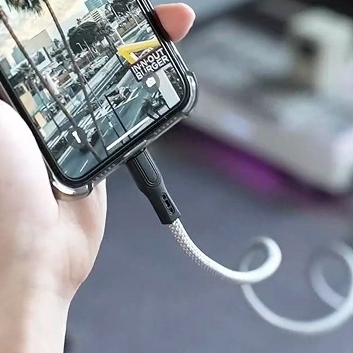 Eine Hand hält ein Telefon mit einer Karte, das über ein weißes und graues Kabel aufgeladen wird.