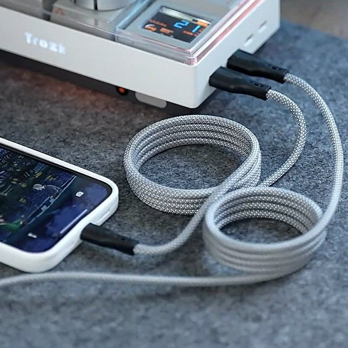 Ein Telefon, das über ein graues Kabel mit einem Ladegerät verbunden ist. Das Ladegerät ist weiß mit Display. Das Kabel ist aufgerollt.
