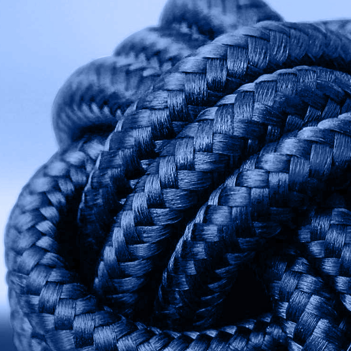 Nahaufnahme eines eng gewickelten, dicken blauen Seils. Die Textur des Seils ist aufwendig gewebt, mit Schatten, die Tiefe verleihen. Himmel im Hintergrund.
