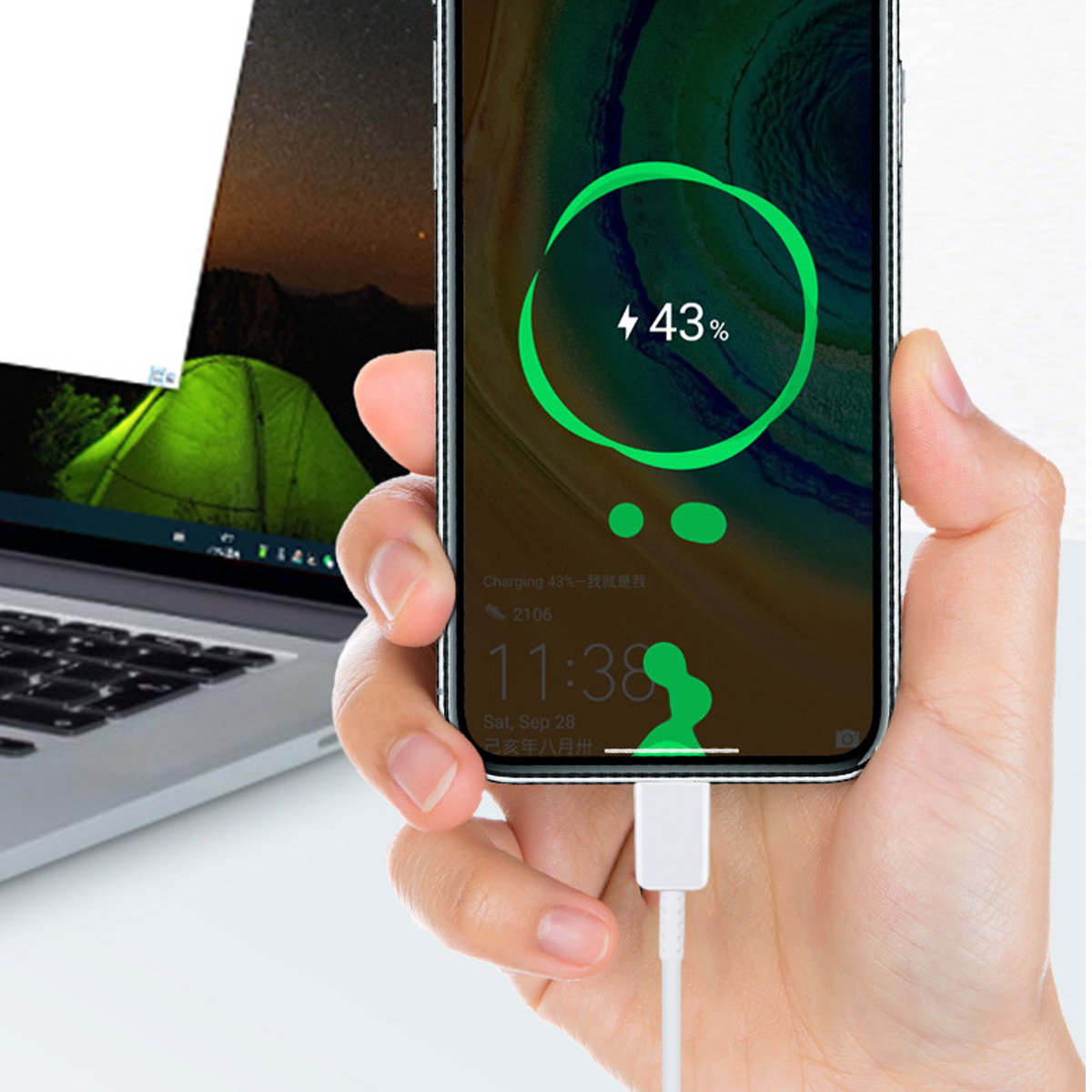 Eine Hand hält ein Telefon, das zu 43 % geladen wird. Im Hintergrund ist ein Laptop mit einem grünen Zeltbild zu sehen.