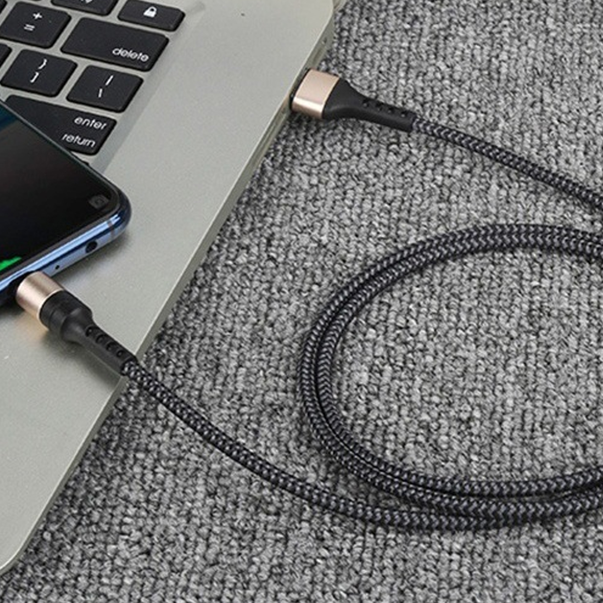 Ein Telefon und ein Laptop sind durch ein Ladekabel verbunden. Das Kabel hat einen schwarzen und goldenen Stecker.