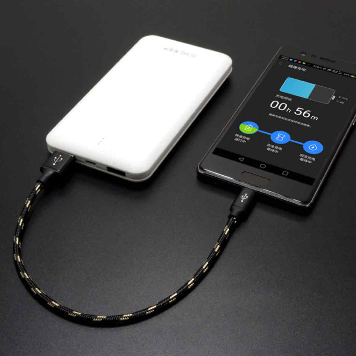 Eine weiße Powerbank und ein schwarzes Smartphone sind durch ein Ladekabel auf schwarzem Untergrund verbunden.