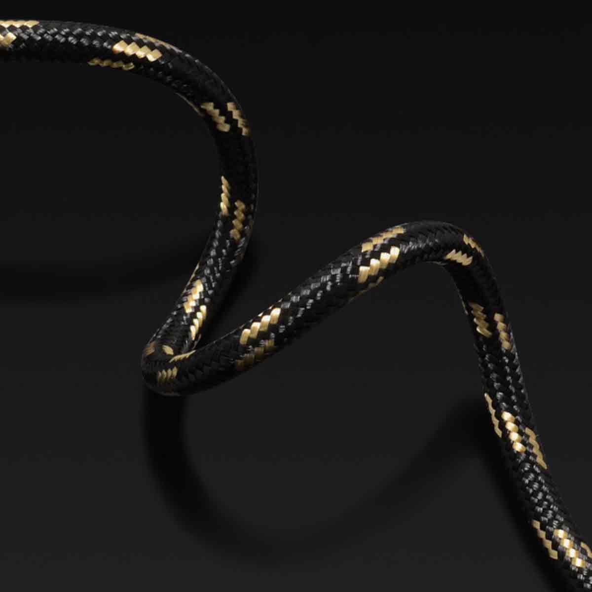 Nahaufnahme eines schwarz-goldenen geflochtenen Kabels, das sich vor einem dunklen Hintergrund krümmt. Das Kabel hat ein strukturiertes Muster.